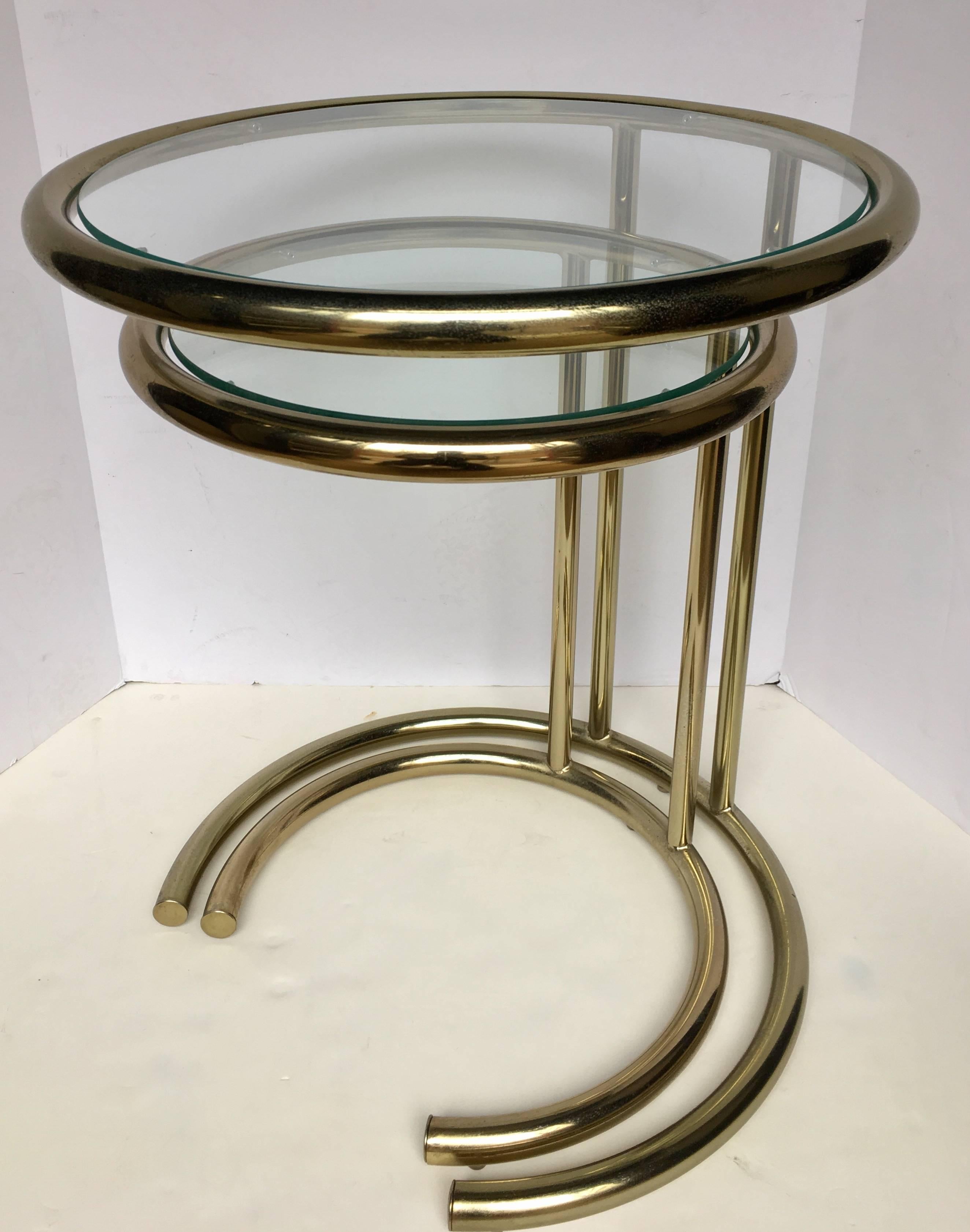 Set of two Mid-Century Modern brass-plated nesting accent tables in the style of Eileen Gray. Each end or side table features a tubular metal frame with removable round clear glass inserts. 

Large table: 21.5 H, 18 D
Small table: 19 H, 14.5 D.