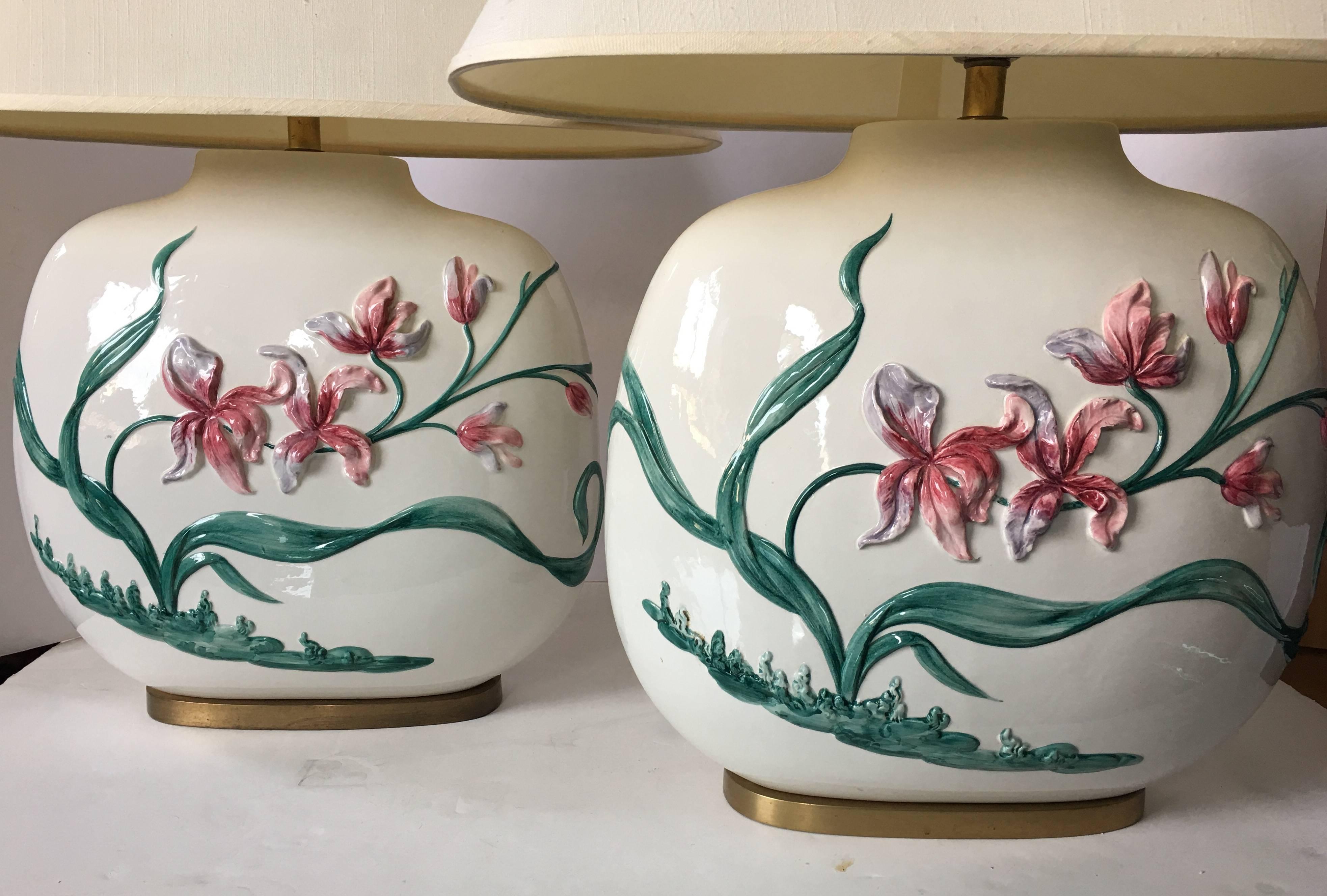 Beautiful pair of chinoiserie style hand-painted floral motif table lamps by Chapman. Oval shaped glazed ceramic bodies feature a dimensional two-sided flowing floral design and brass bases. Original oval shaped lamp shades included. Origonal