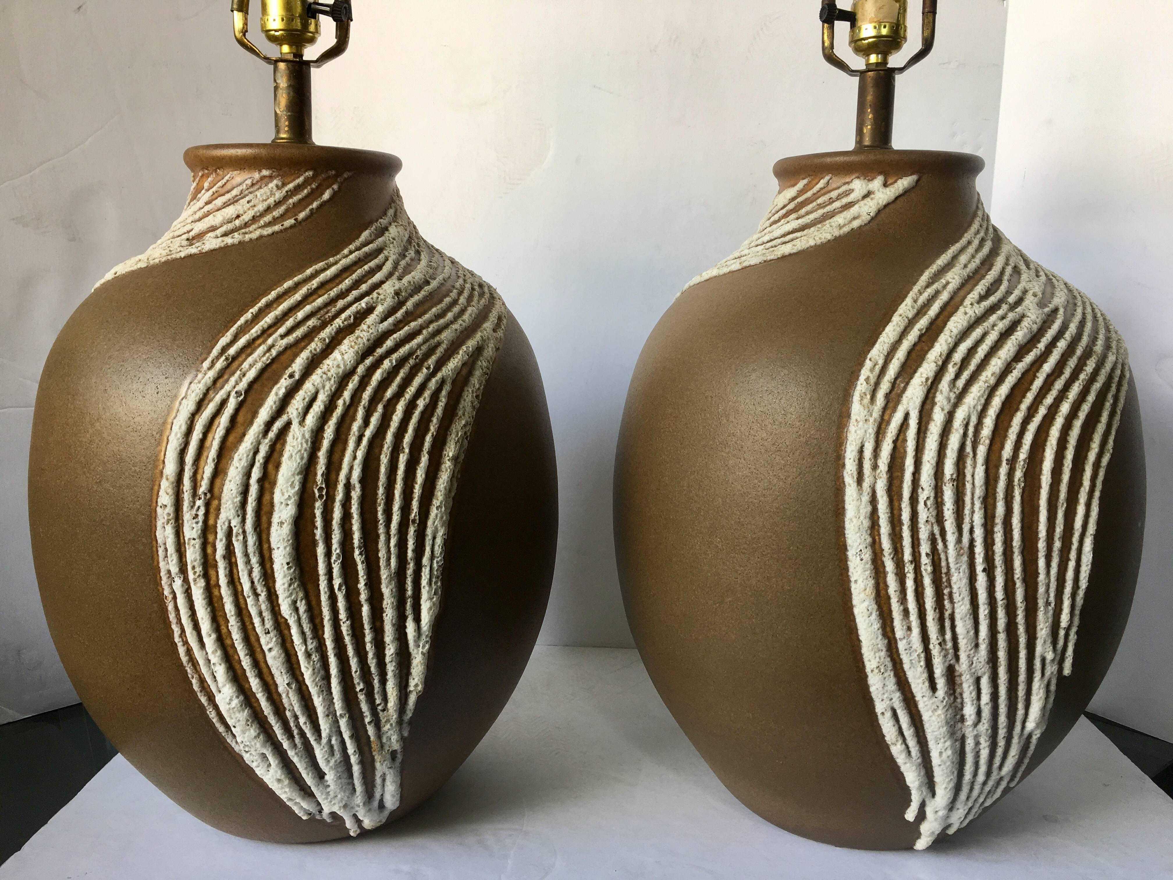 Sizable pair of Mid-Century Modern lava glazed drip pottery table lamps. Matte brown tone ceramic glazed bases feature a white dimensional lava/volcanic textured drip glaze.

Measures: Height to harp 32 inches high.
Height to socket 22 inches