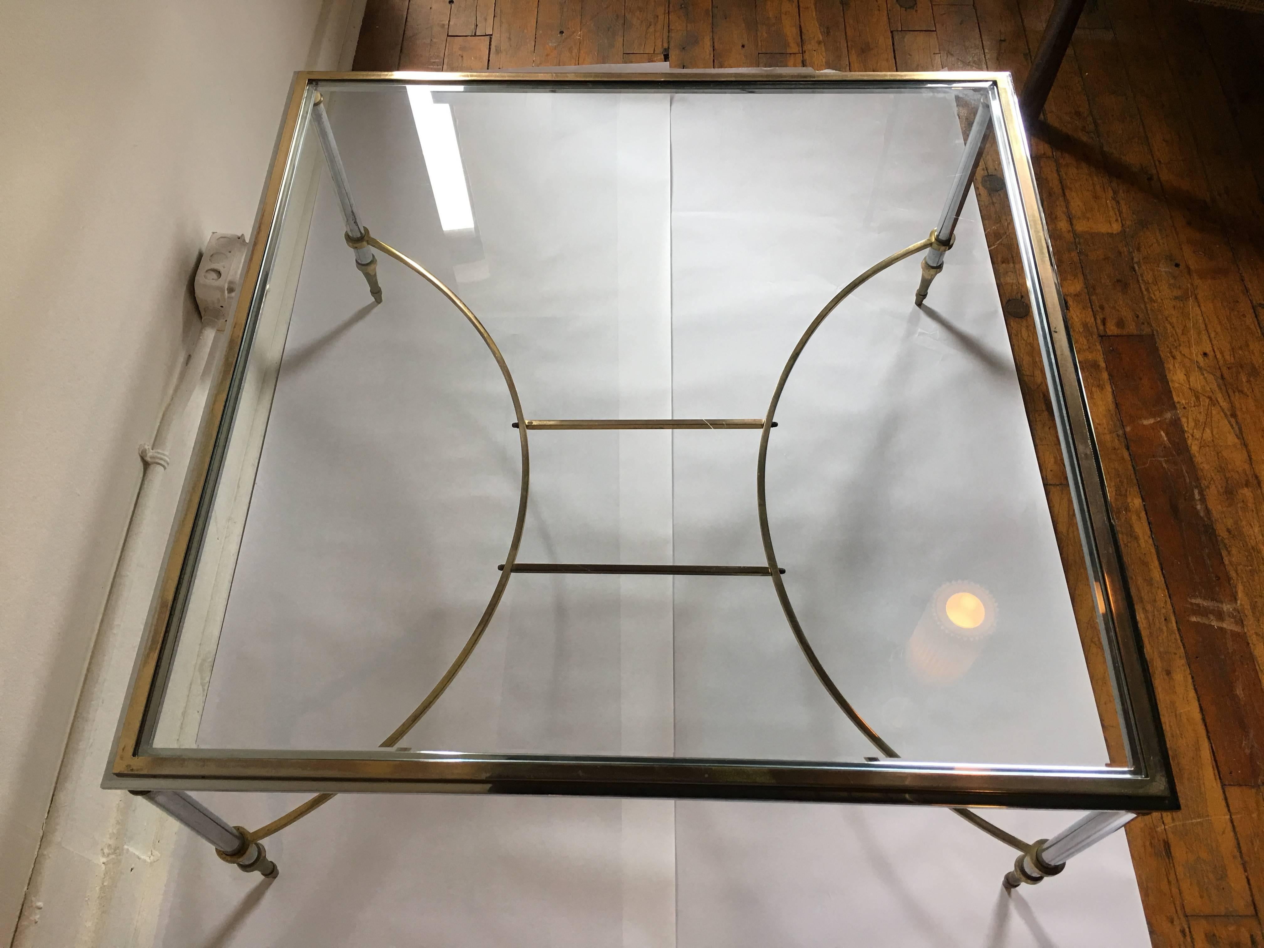 Large Mid-Century Modern beveled glass-top cocktail table in the style of Maison Jansen.  Brass and polished steel chrome square metal frame features curved stretcher base with decorative Regency-style details.  Made in Spain.