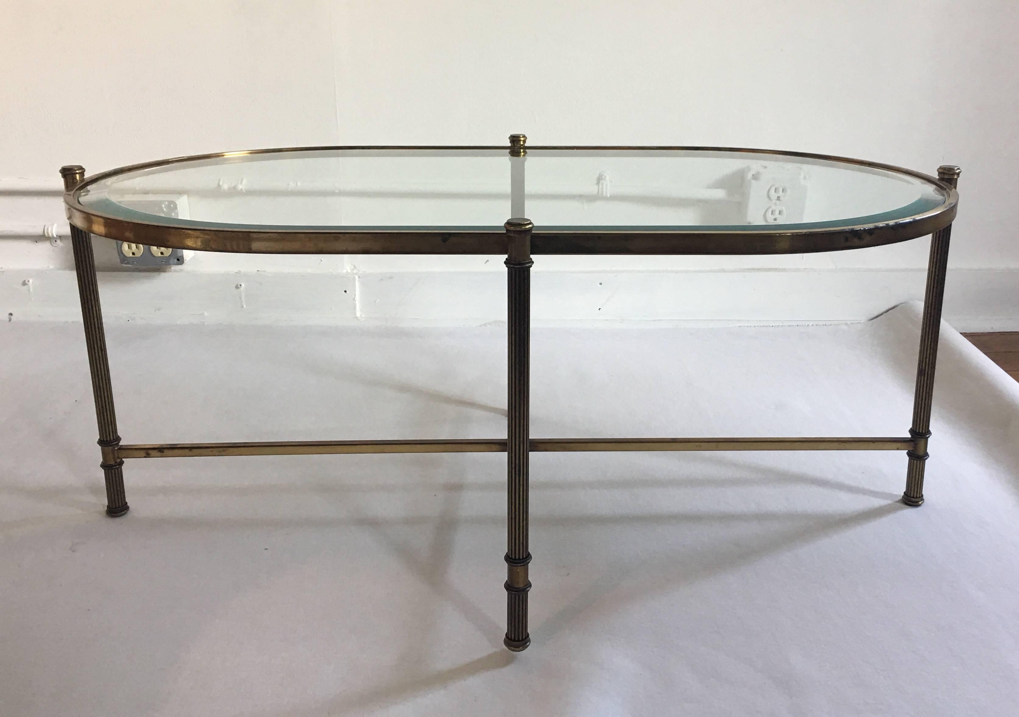 Mid-Century French Maison Bagues style brass and glass coffee table. Curved oval shaped base features fluted legs and a beveled clear glass top.  In the style of Maison Jansen.  