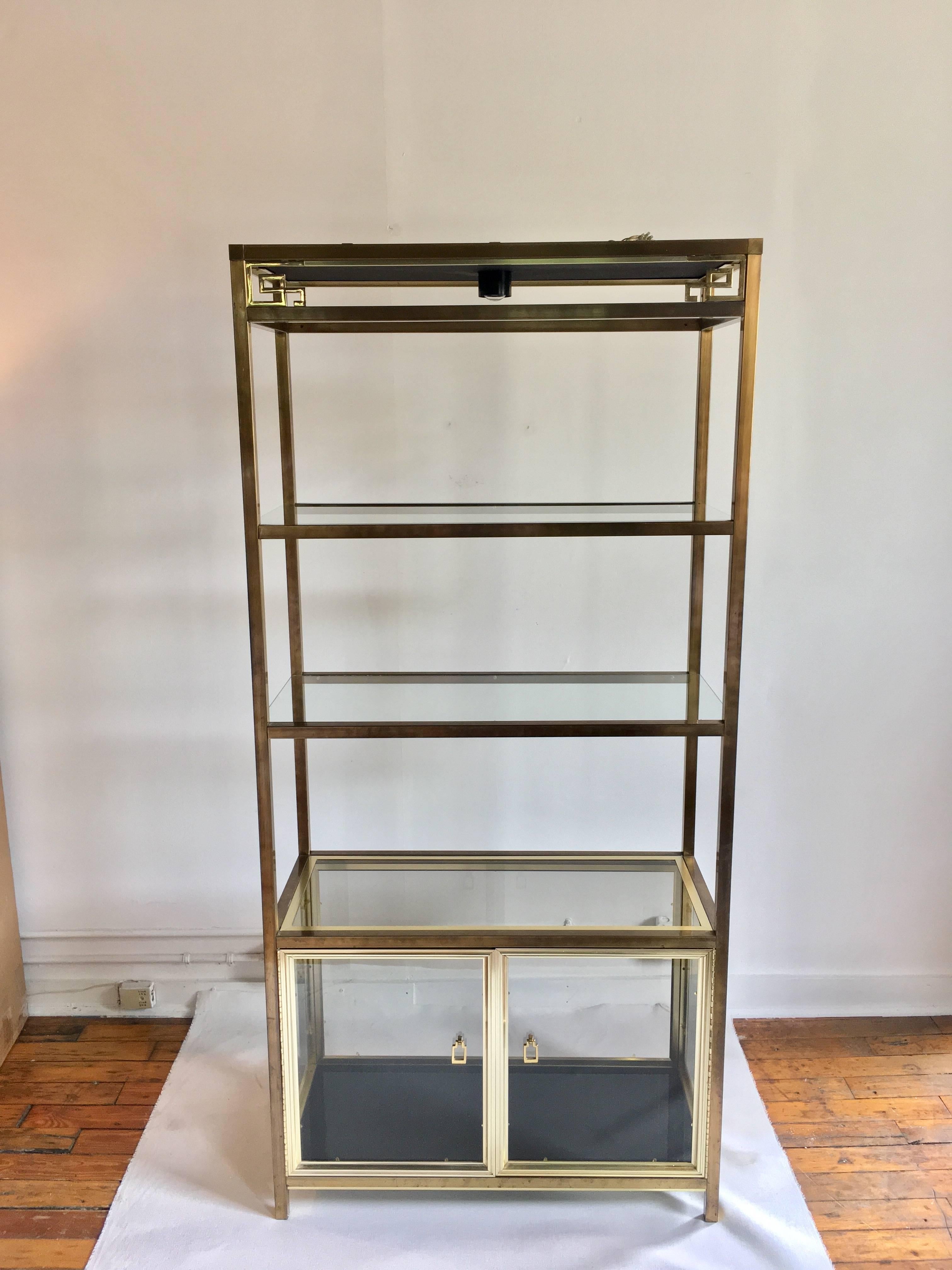 Mid-Century Modern Hollywood Regency style brass and glass étagère shelving cabinet in the style of Mastercraft. Brass gold frame features an Asian/chinoiserie motif with three clear glass shelves and a black glass bottom shelf. Bottom section of