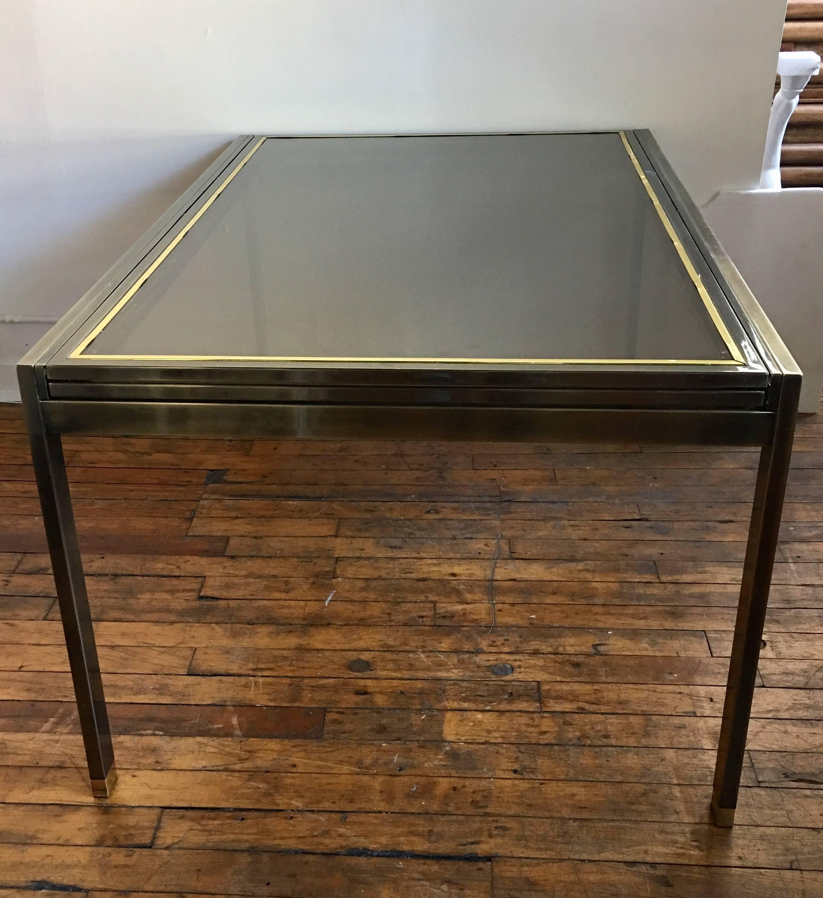 Mixed metal patinated and polished brass and glass extension dining table, Mastercraft Directoire style. Neoclassical style X-form Mid-Century Modern design featuring a draw leaf extension feature that makes this smoked glass table one very long