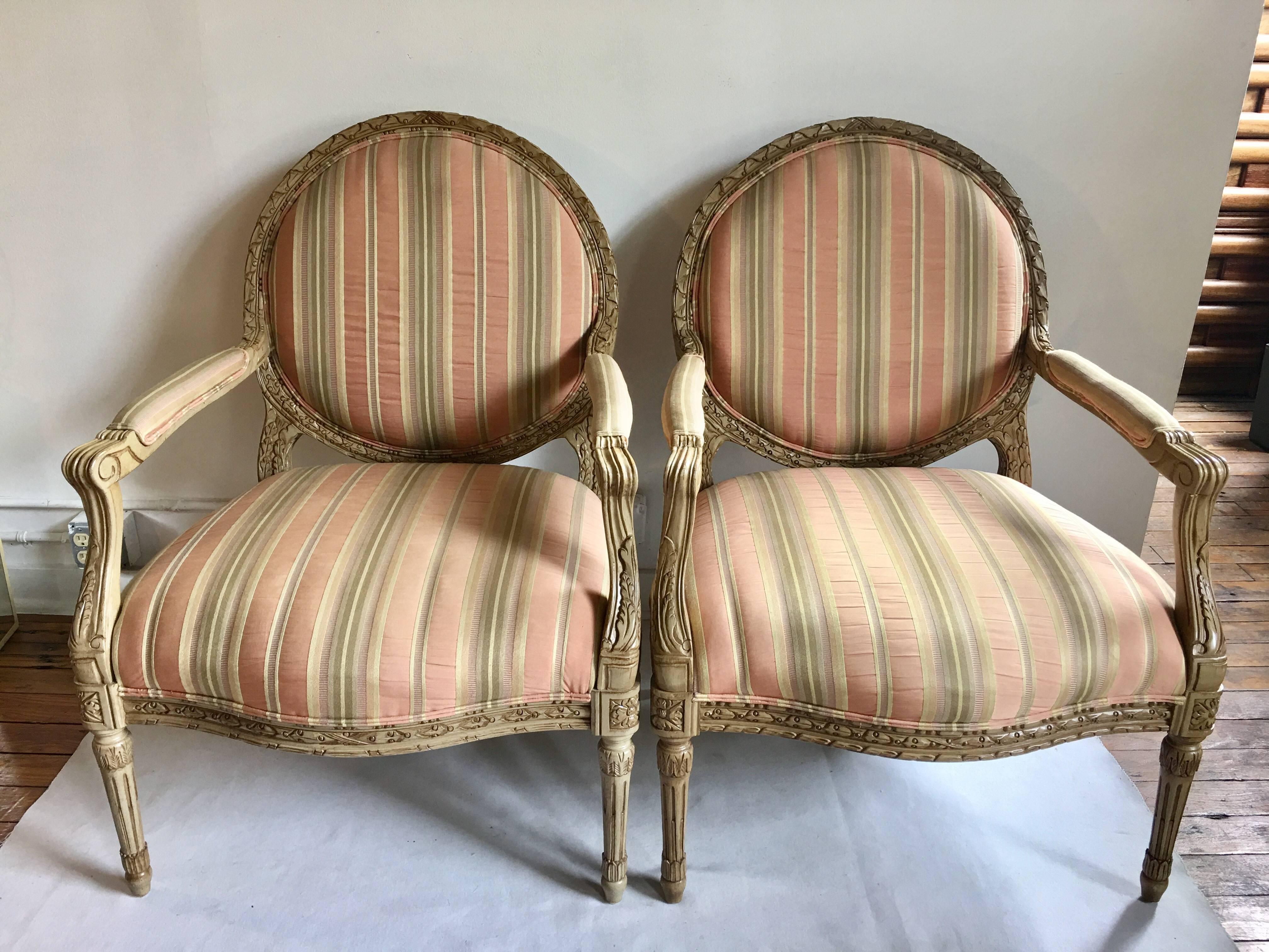 Pair of vintage French XVI style bergère armchairs by Henredon Fine Furniture. These generous sized accent chairs feature carved relief painted wood frames with a traditional round medallion shaped back and neoclassical style fluted legs. Chairs are