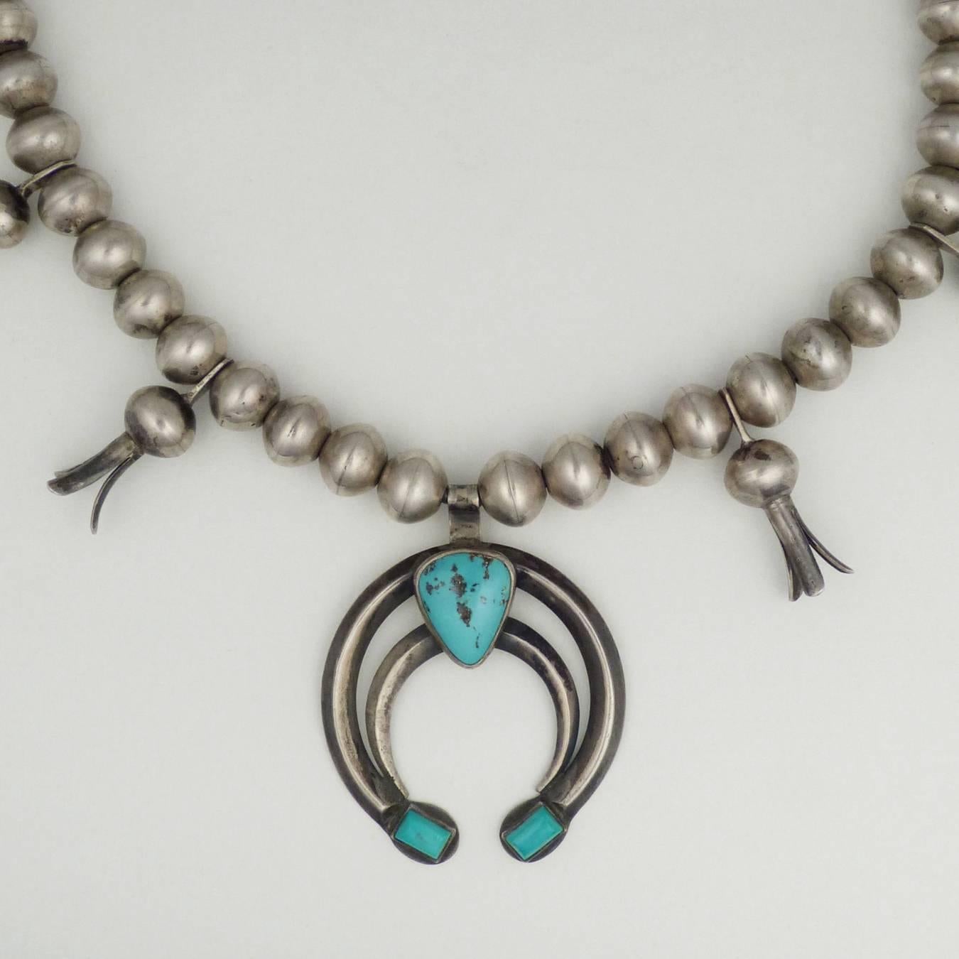 The squash blossom necklace is an iconic piece from the American southwest. This necklace is a perfect example, with its central naja adorned with three bezel set natural turquoise stones. Necklace measures 23