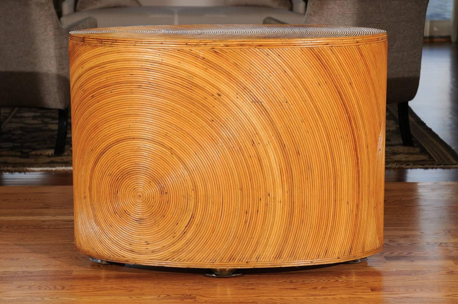 A stunning fixed console, circa 1970. Fabulous oval mahogany construction, painstakingly veneered in pencil bamboo. The piece is mounted atop stylish brass feet. Swirling sunburst motifs accent the sides and top. Exceptional style, quality and