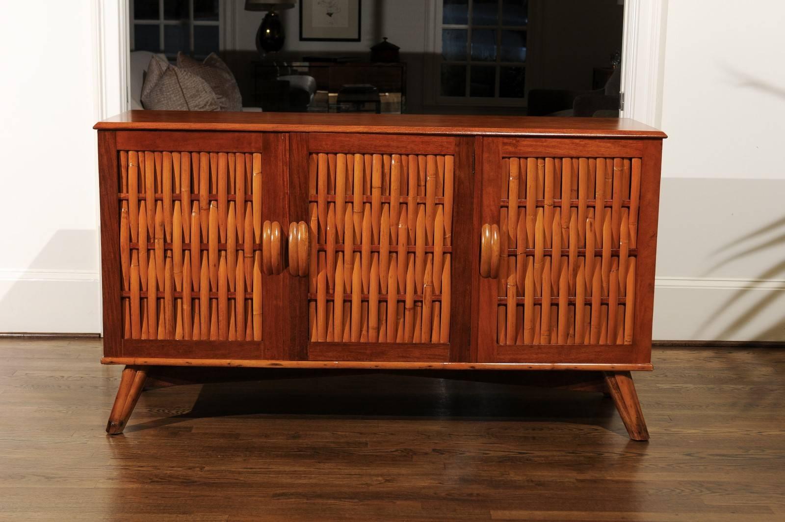 A stunning restored cabinet or buffet, circa 1940. Expertly crafted solid mahogany case construction with basket weave inset doors fashioned from strips of bamboo. Base is comprised of rattan feet connected with mahogany stretchers. Simple rattan