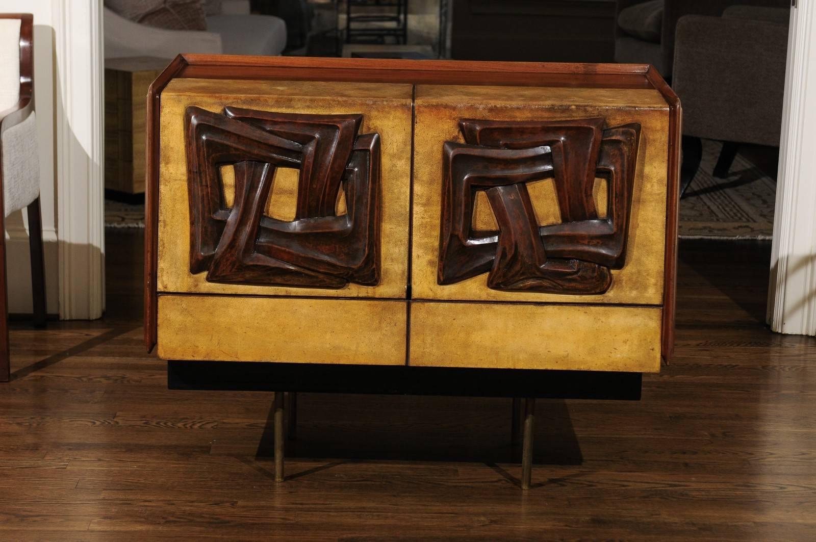 A stunning bar cabinet attributed to Claude Vassal, France, circa 1950. Striking wedge shaped rosewood case with drop-front doors clad in goatskin. Magnificent hand-carved Walnut motifs adorn the doors. The cabinet is mounted atop simple solid brass
