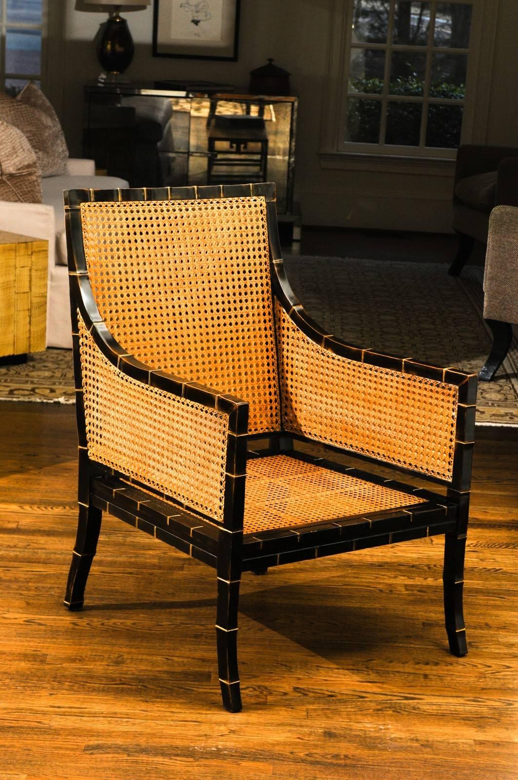 A stunning pair of double sided cane club chairs, circa 1970. Handsome large scale ebony form with faux-bamboo detail accented in gold leaf; subtle Klismos leg detail. Heavy, expertly crafted and aged to absolute perfection. Pieces designed to
