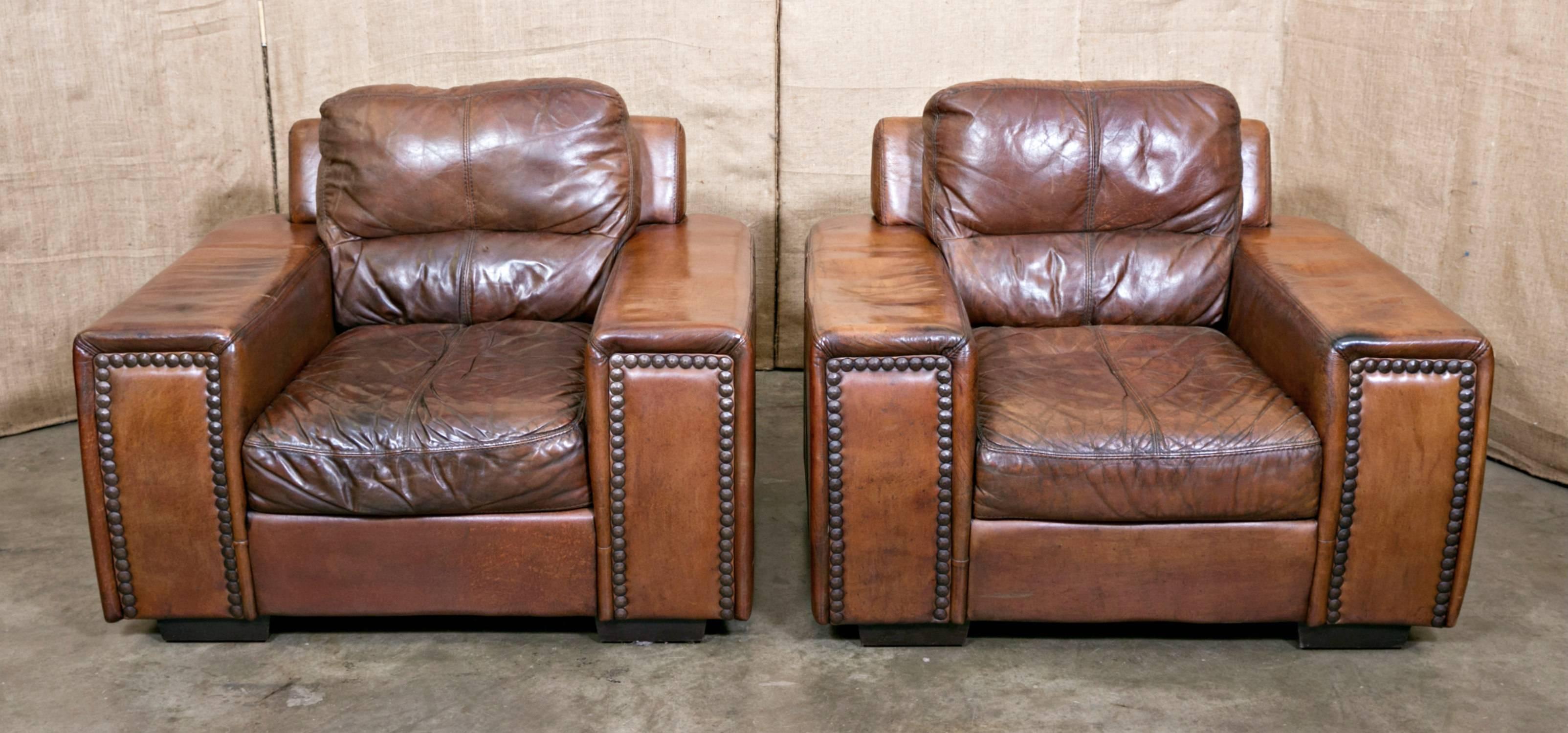 These ultra-cool 1970s French club chairs in handsome brown leather burnished to vintage perfection will add character and style to any decor. They're possibly the most comfortable pair of chairs ever, having large sturdy arms with nail head trim