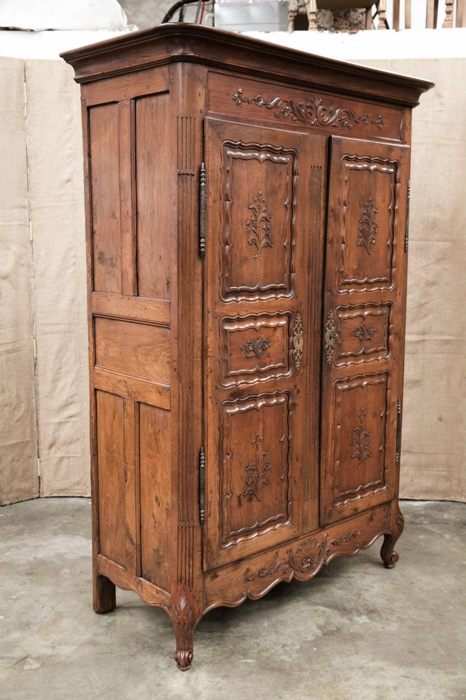 Intricately carved early 19th century Country French Louis XV style armoire handcrafted by skilled artisans in the Breton region of France from old growth oak. The cornice sits atop a carved frieze featuring motifs such as flowers, leaves and