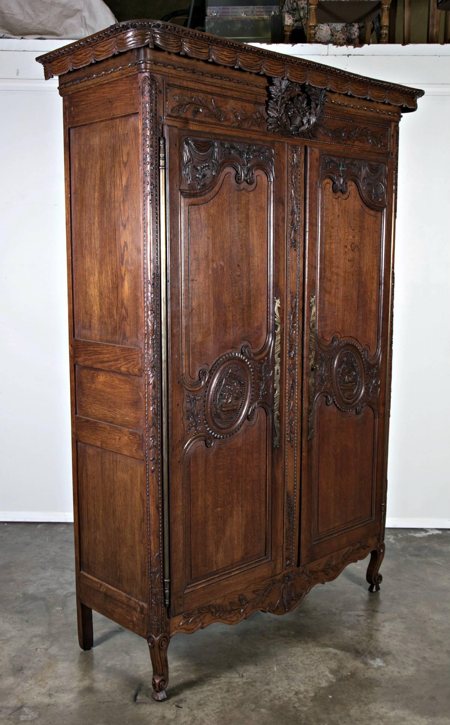 Antique French Louis XV style solid oak marriage armoire having a rare hand-carved drapery crown above a frieze that features a basket of flowers. Paneled doors highlighted with floral and foliate carvings above a scrolled and accented apron. Raised
