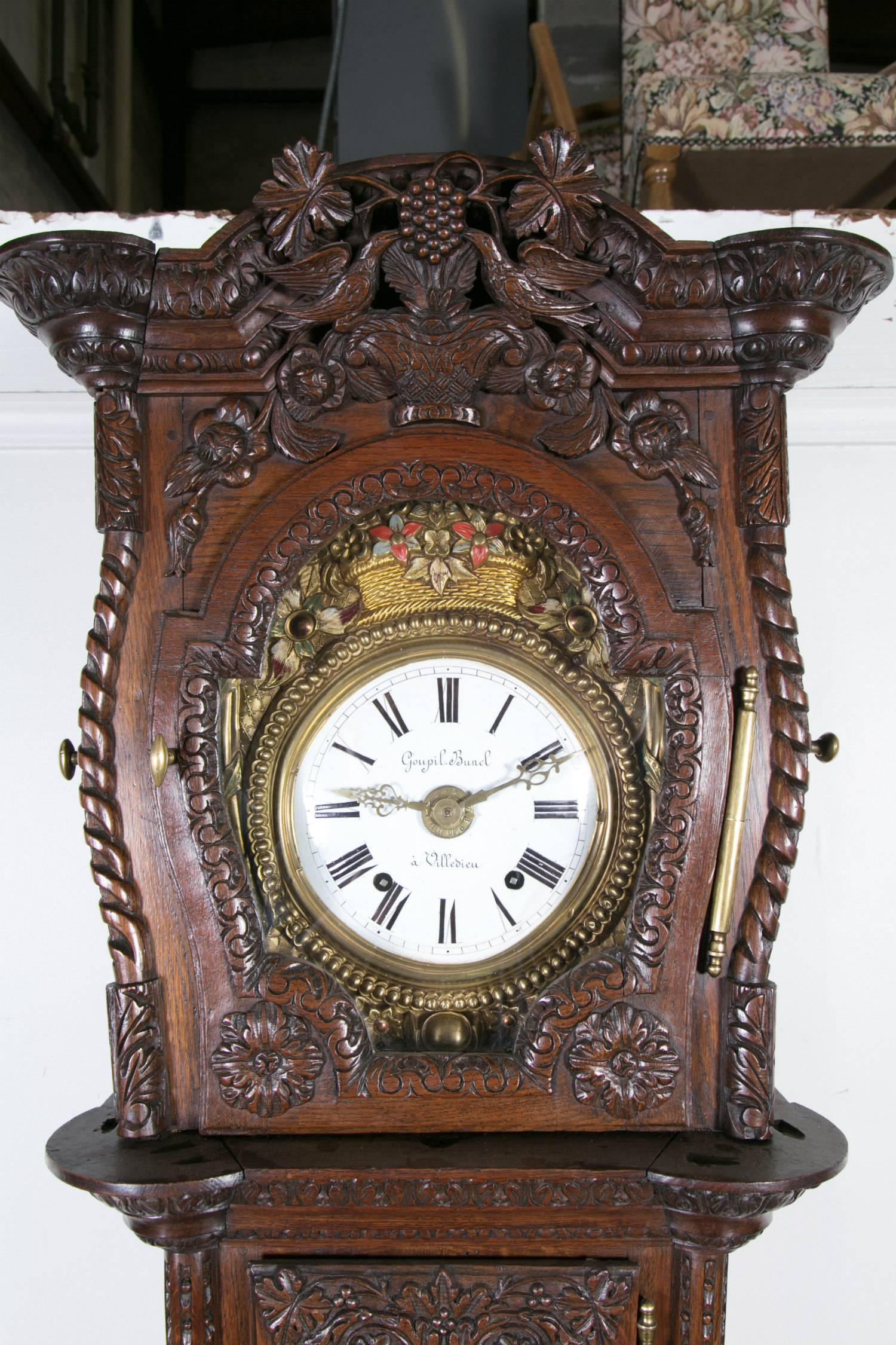 Rare pendule de grande taille de style Louis XVI, datant du début du XIXe siècle, qui aurait fait partie de la dot d'une jeune mariée à l'occasion de son mariage. Elle est dotée d'un mouvement à comtoise de huit jours, en chêne mouluré et sculpté,
