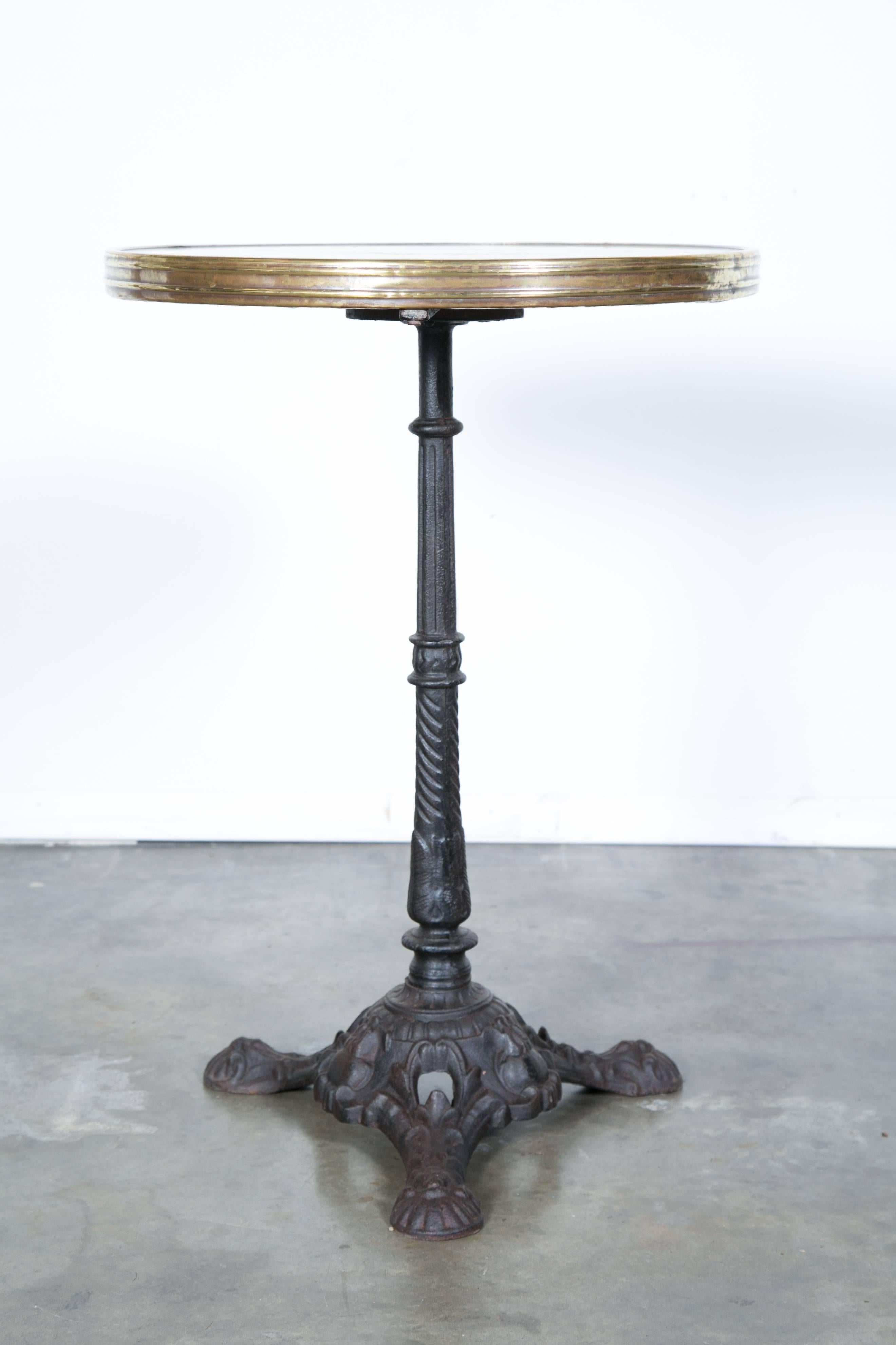 Charming antique Parisian bistro table with a beautiful cast iron base and marble top with brass trim. The iron tripod base is done with a classic styling and a marvelously aged patina. The marble top also boasts a wonderful weathered patina from
