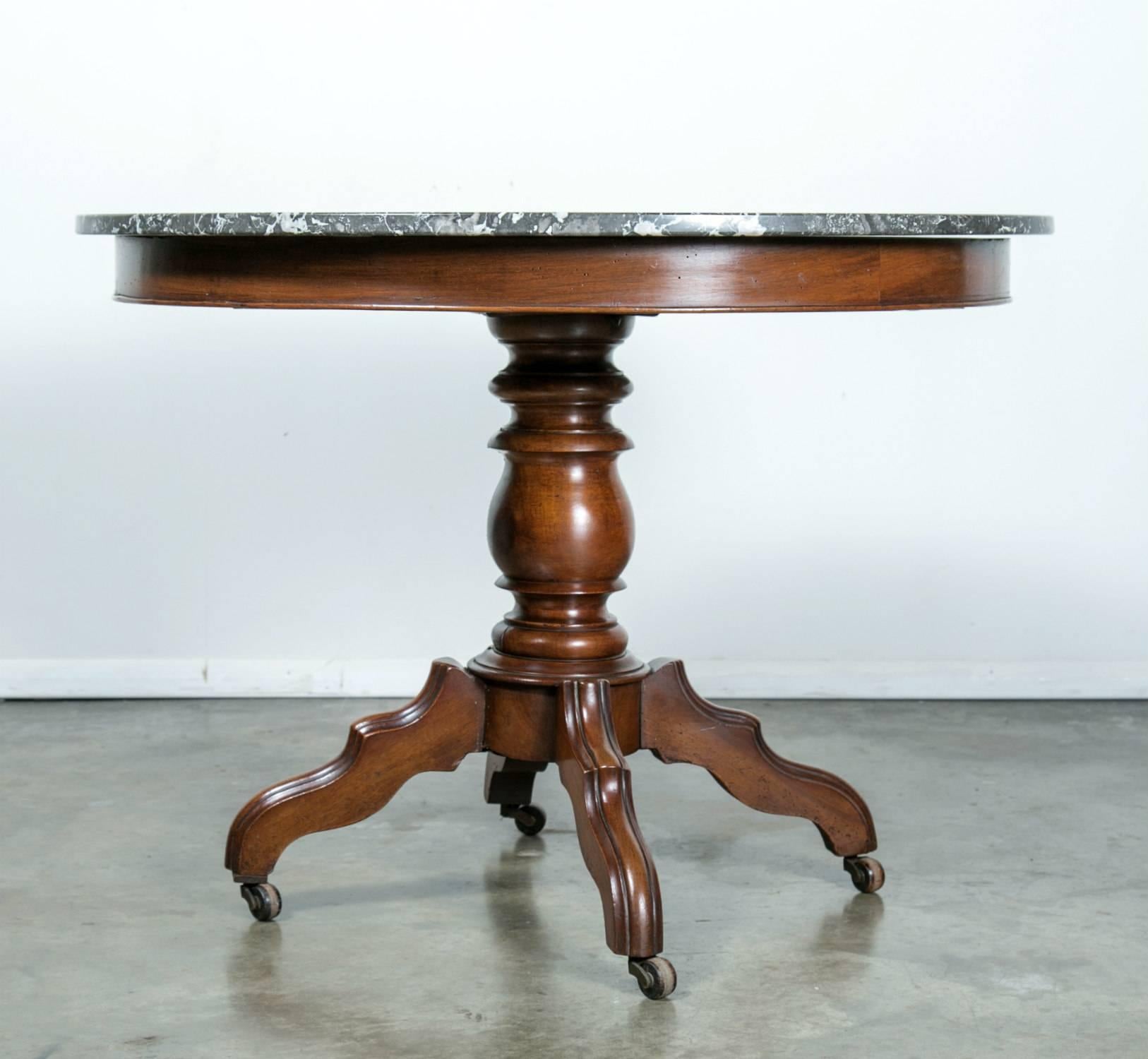 Elegant French Louis Philippe period gueridon or center table having a high polished gray Saint Anne marble top with white veins. Raised on a baluster turned solid walnut pedestal on four hand-carved legs, on casters.