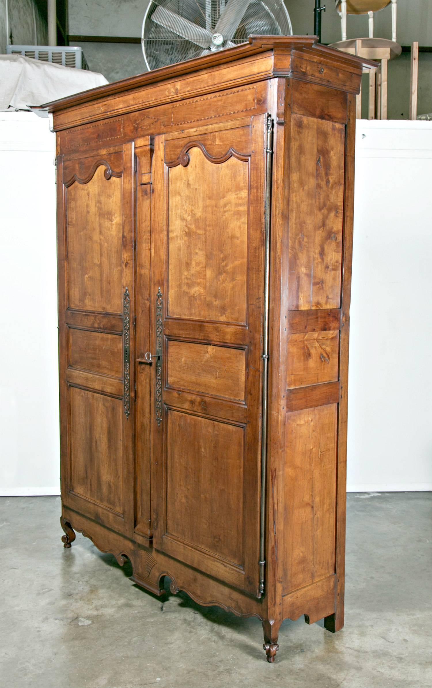 Monumental 18th century Louis XV period carved armoire handcrafted of wild cherrywood by highly skilled rural artisans, having an ogee canted corner crown above a fruitwood inlaid frieze. The triple paneled doors, separated by a relief pilaster,