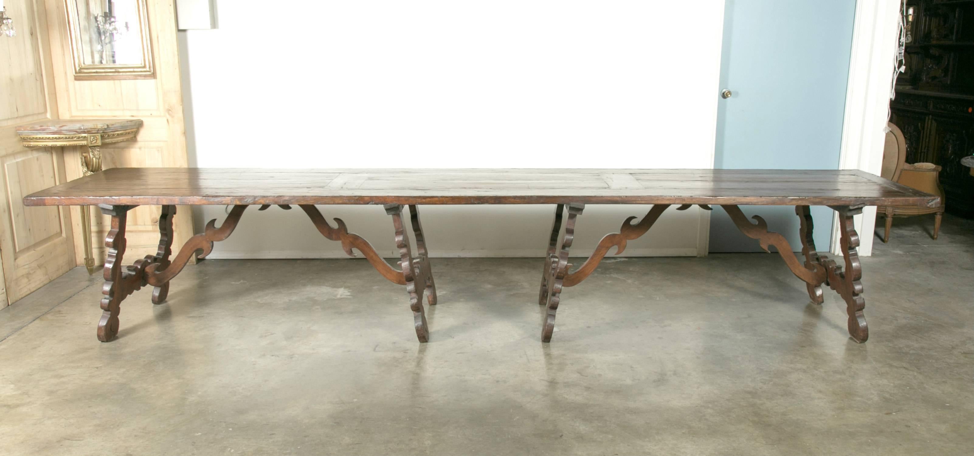 A monumental early 19th century Italian trestle table, having a rectangular framed solid walnut inset board top, resting on four hand-carved, classical lyre legs joined by four beautifully carved pair of wood S-scroll stretchers.

This unique
