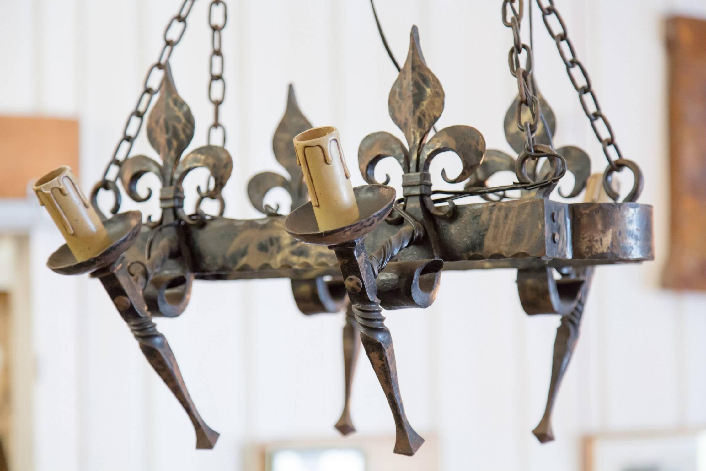 Hand-forged iron four-light Country French chandelier with wonderful patina. This oval chandelier with fleur de lis details and four torchere style mounts holding wax candle sleeves will add rustic charm to any space. The four lights are joined in