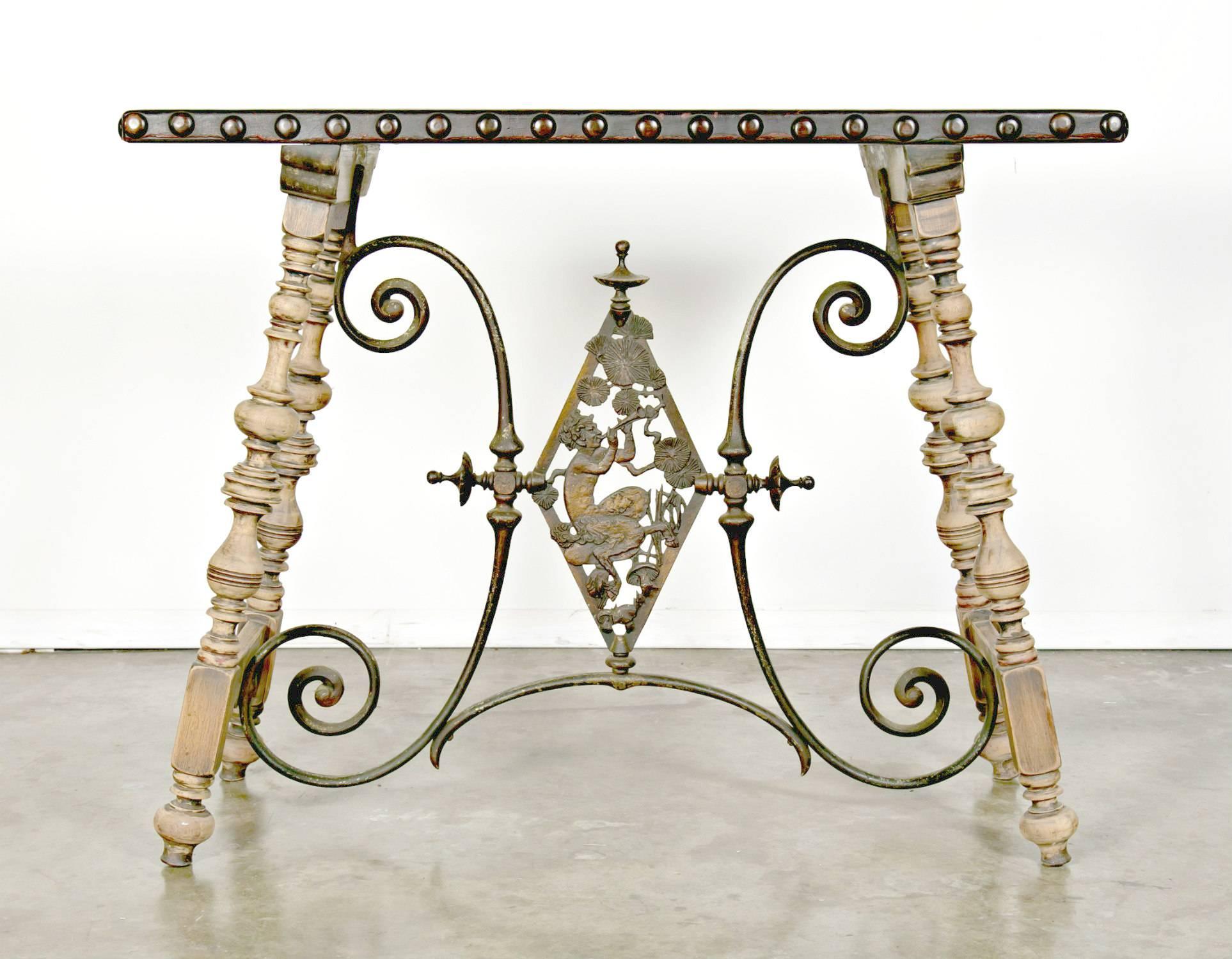 Wonderful 1920s Oscar Bach Art Deco console, having a leather top with large nailhead trim. The turned walnut legs, joined by a cast iron stretcher with a bronze patina and embellished with an ornate satyr motif, show traces of original polychrome.