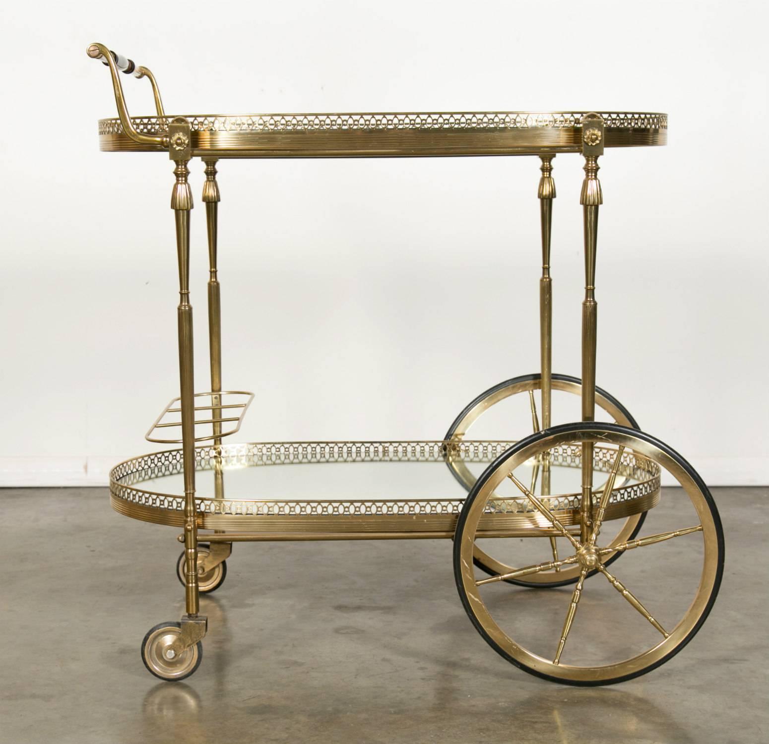 Vintage French two-tier oval brass faux bamboo bar cart, drinks or serving trolley by renowned French design house Maison Baguès, having top glass tray and mirrored bottom tray, each with pierced galleries, with brass bottle rack for three bottles