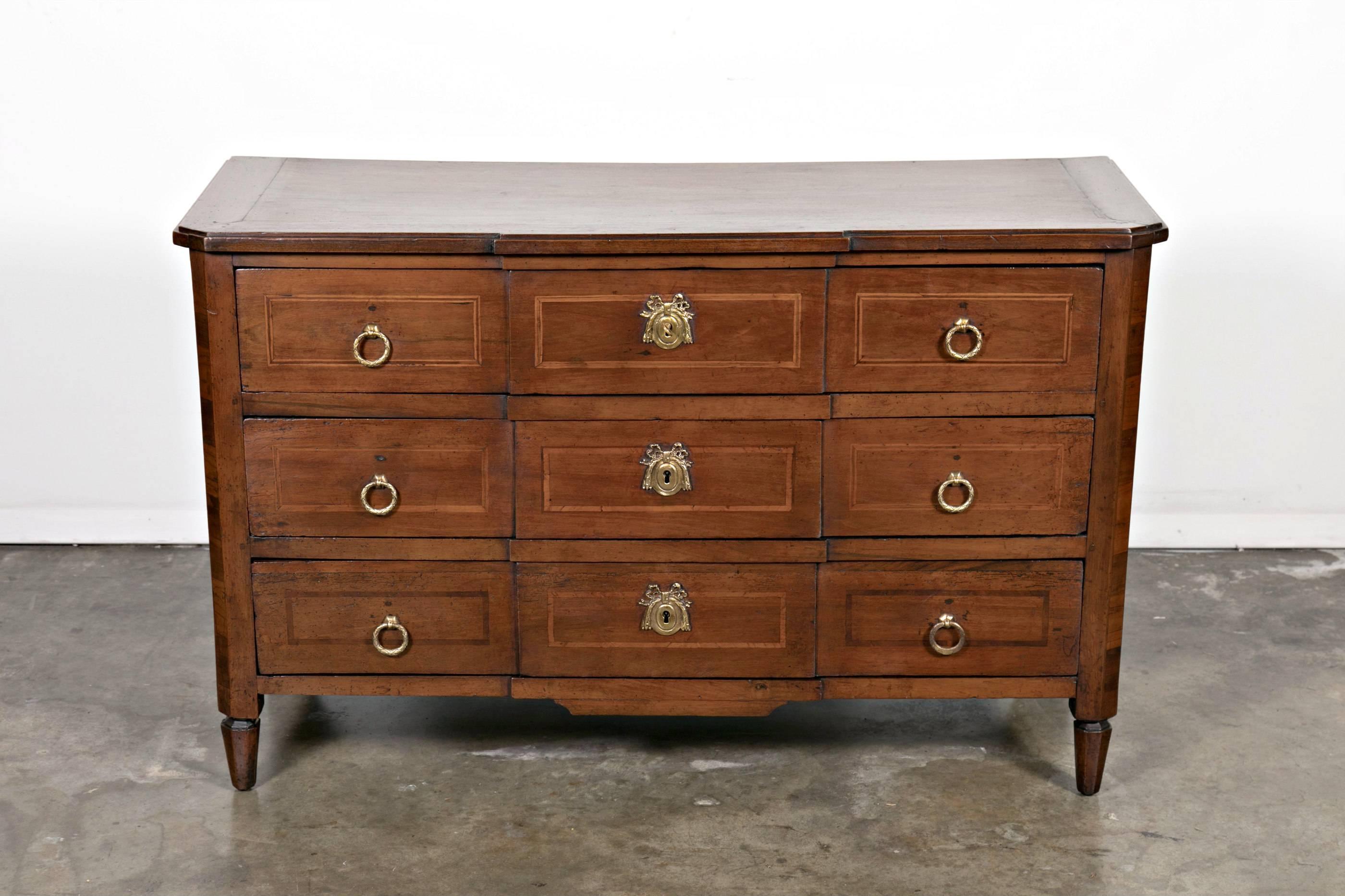 A Fine late 18th century period Louis XVI petite Parisian commode in neoclassical form handcrafted by master artisans in walnut and fruitwood marquetry, having a rectangular top with canted front corners sitting above three drawers adorned with