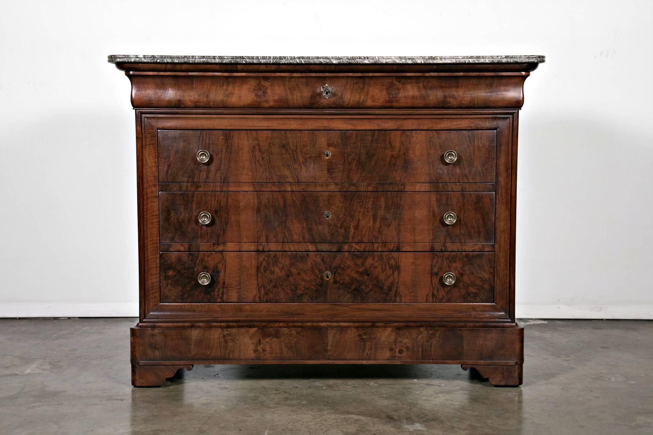 A handsome French Louis Philippe period commode of solid walnut with a bookmatched front. Featuring a Saint Anne ogee marble top above a long doucine drawer with three fitted drawers below, resting upon pistolet feet. The three lower drawers have a