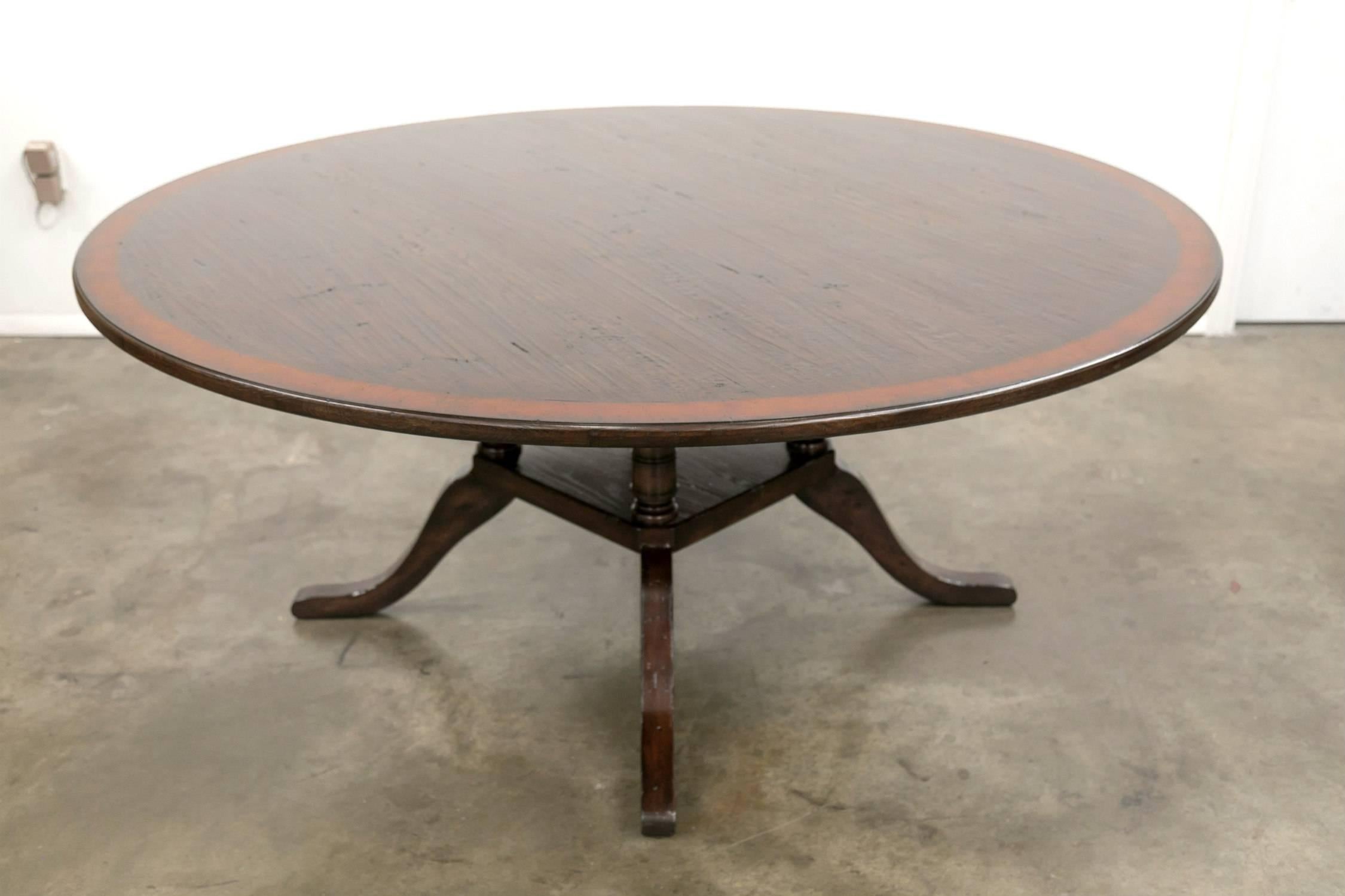 A Classic Georgian style pedestal dining table, handcrafted in England, having a 60 inch diameter, oak top bordered by a rich burled walnut band. Supported by a birdcage pedestal base made of four turned and carved rustic oak columns over a square