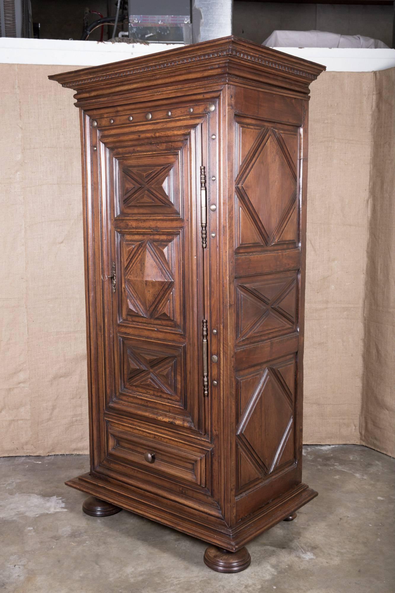 Impressive French 17th century Louis XIII style bonnetiere handcrafted from old-growth French walnut. Stepped out cornice atop a single door with three gem-cut raised panels and large iron nailhead trim above single drawer. Raised gem-cut panels