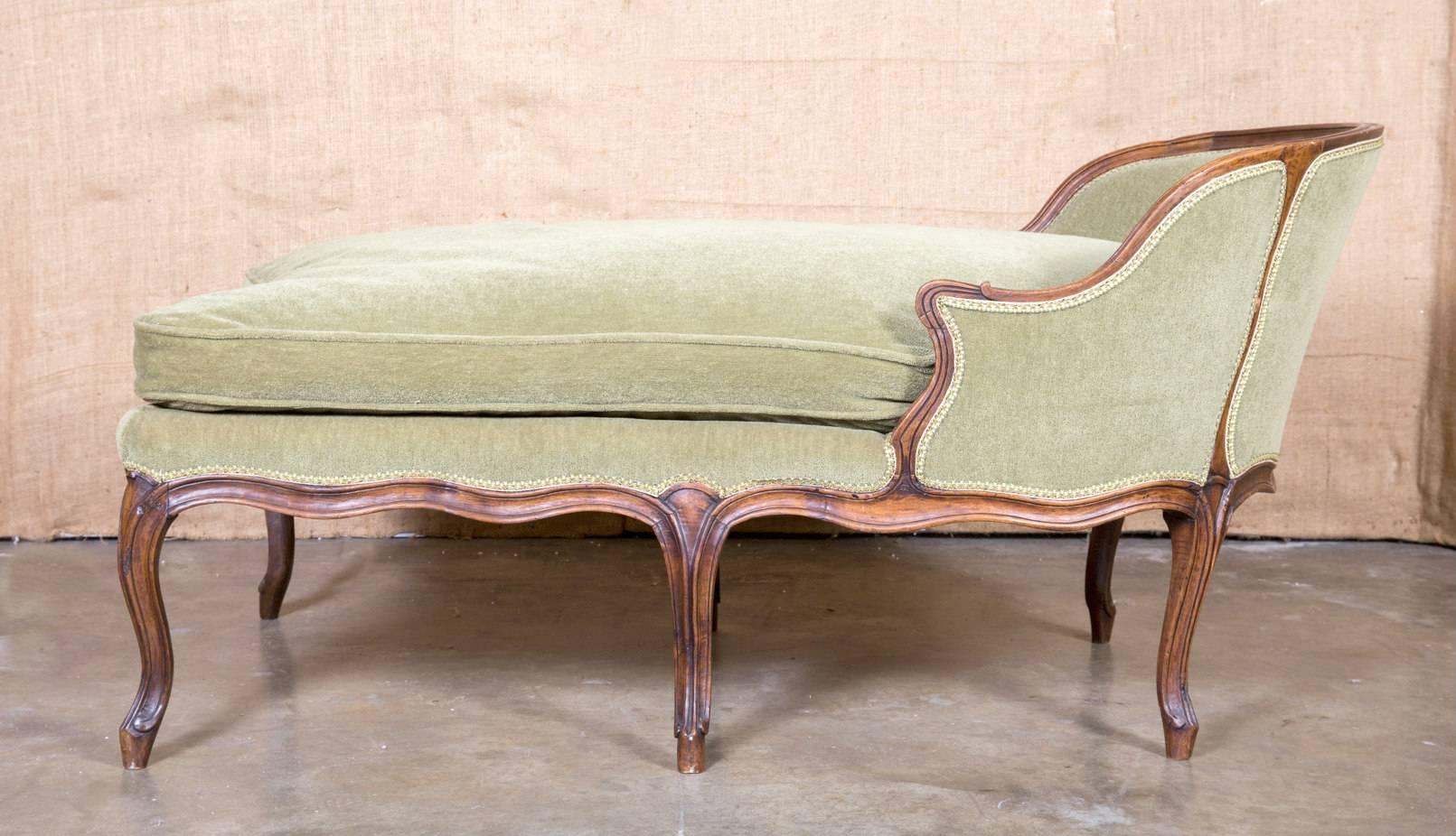Louis XV style petite chaise longue handcrafted in walnut. The seat cushion is a mixture of dawn and feather and the upholstery is in very good condition. Rests over scrolled French toes.