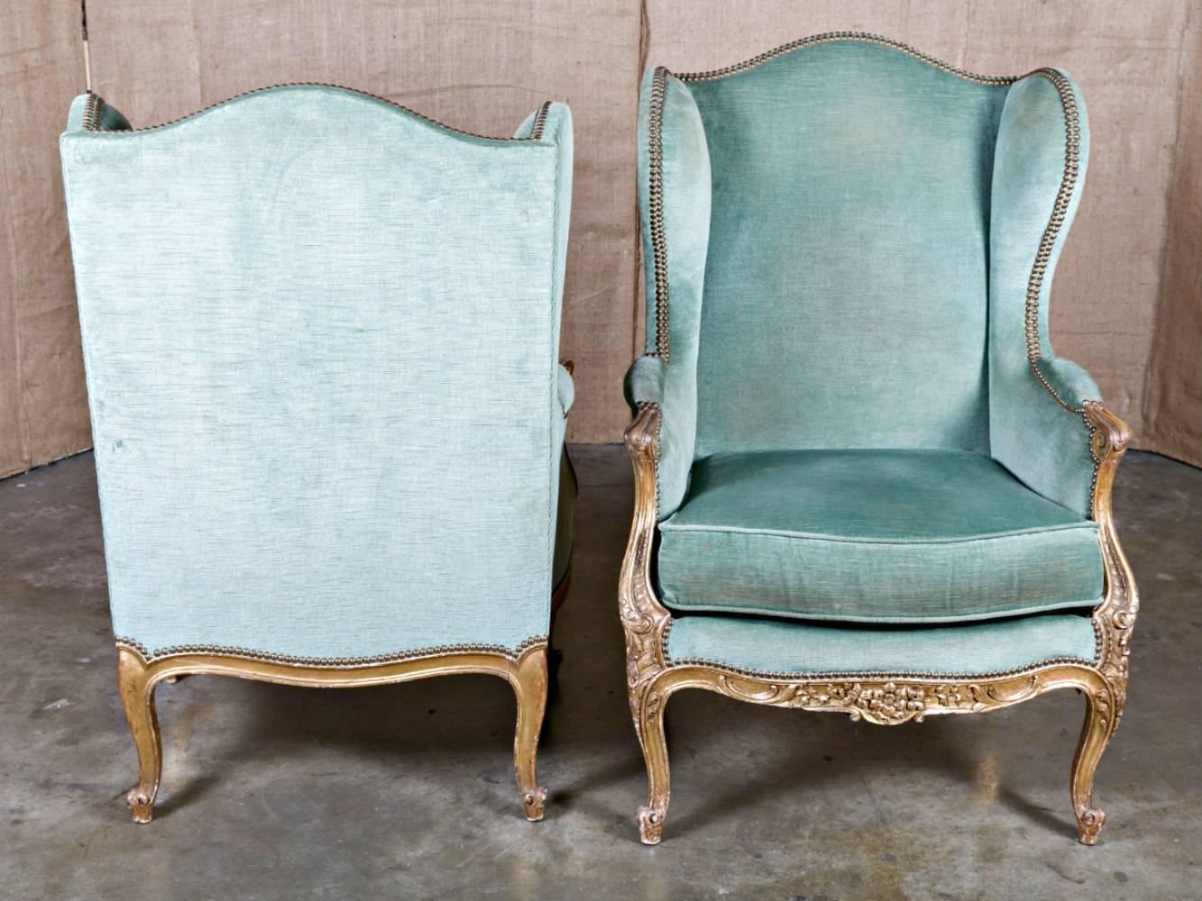 Pair of exceptional 19th century French Louis XV style carved giltwood bergère à oreilles (wingbacks,) having chapeau de gendarme backrests with extending wings upholstered in velvet with brass nailhead trim. Down filled cushions flanked by