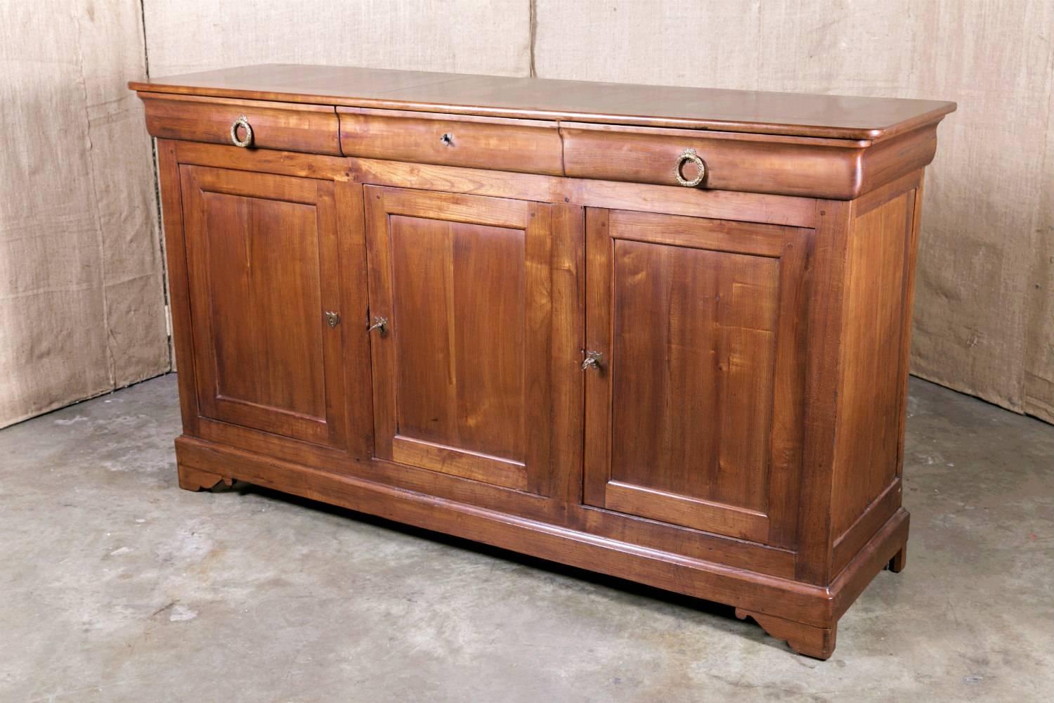 French Louis Philippe period enfilade handcrafted of solid cherry by skilled artisans in the Brittany region, having three doucine drawers over three paneled doors with original bronze pulls. Resting on shaped bracket feet. 

This handsome