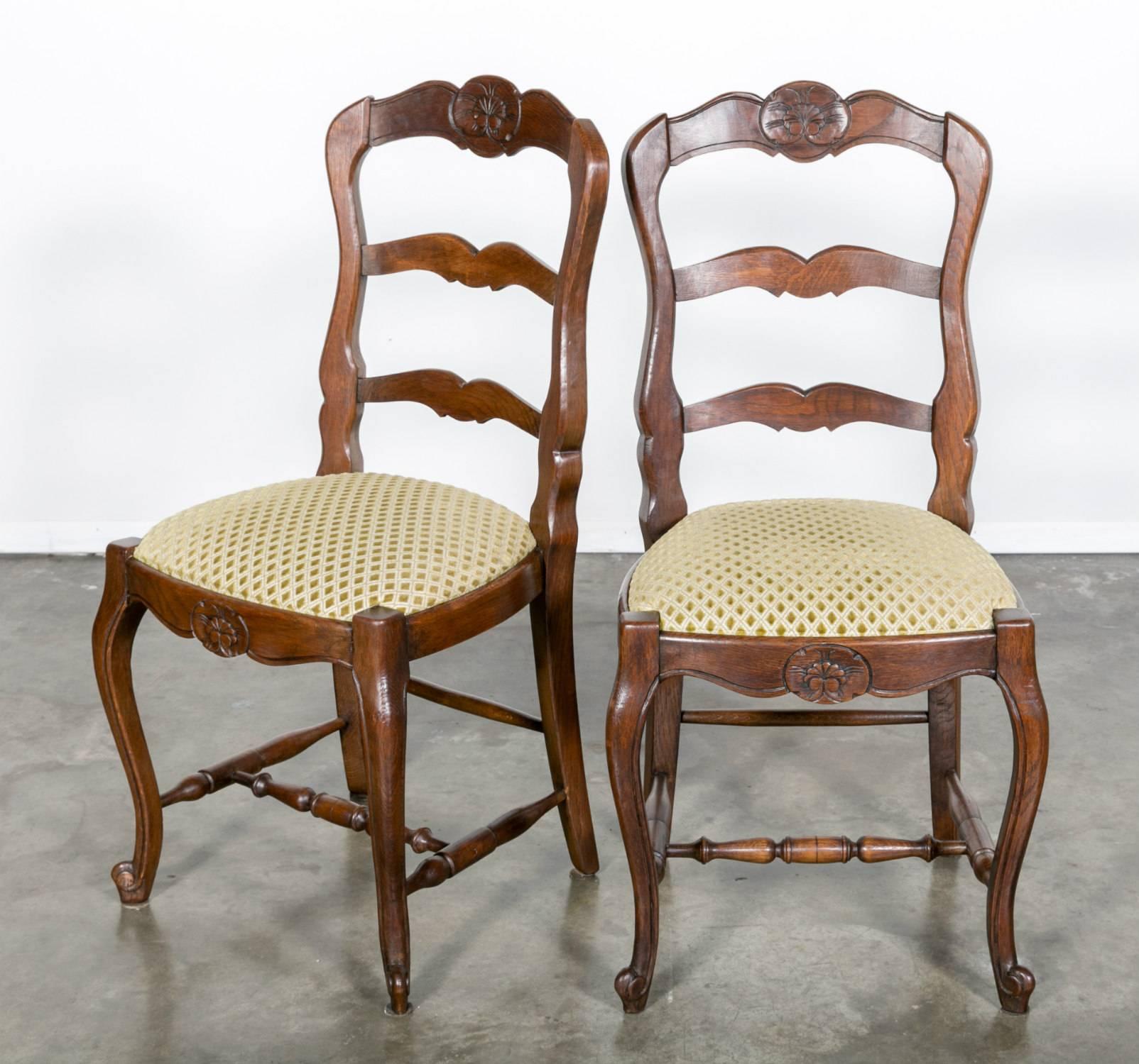 Set of six Country French dining chairs with upholstered seats and typical Louis XV motifs. Handcrafted from solid oak, this charming set dates from the early 1900s. Each chair is decorated with floral motifs on the crest rail and apron. The front
