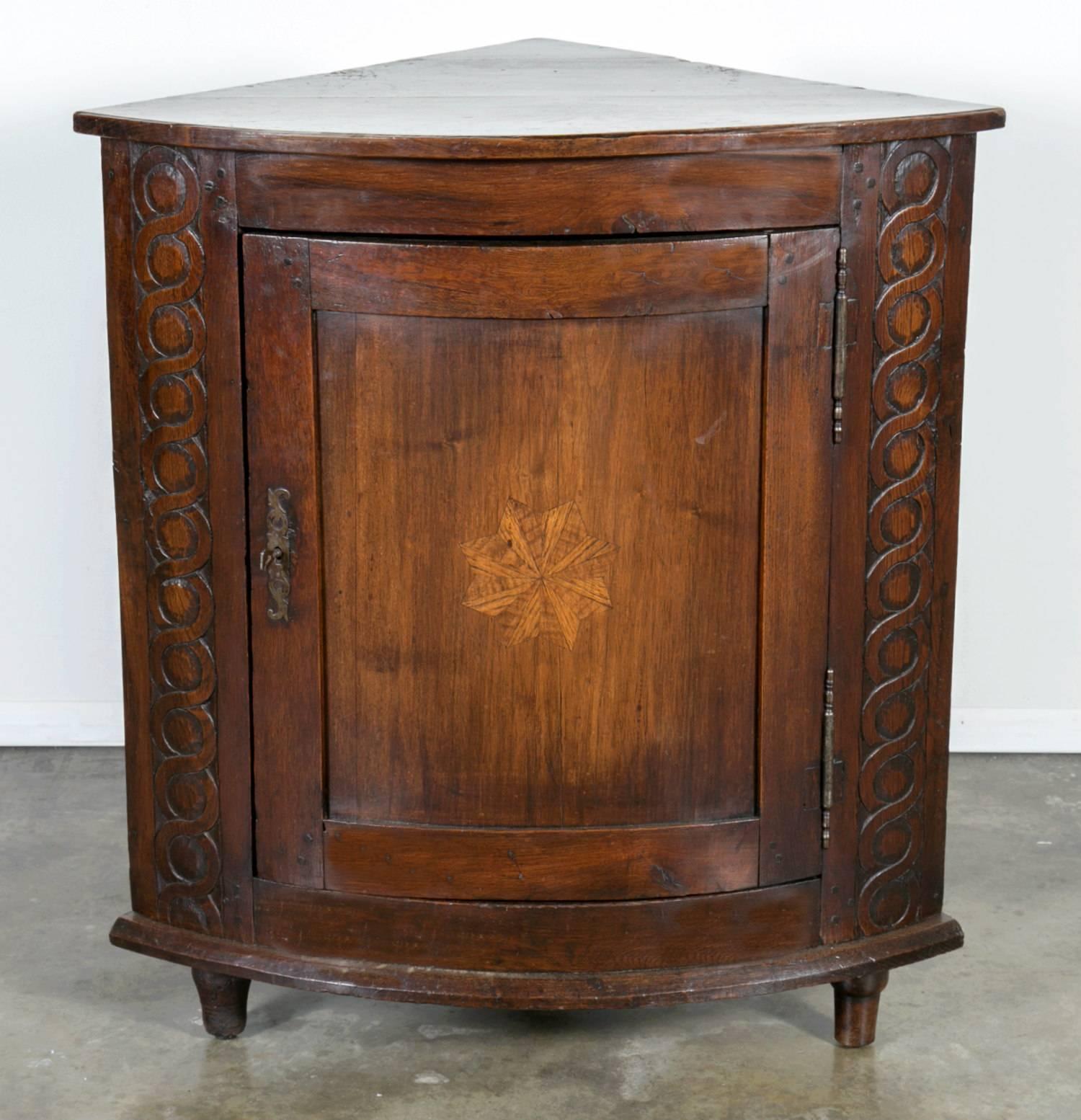 18th century Country French encoignure or corner cabinet handcrafted of solid oak by talented artisans from Normandie. This corner cabinet, with carved spirals and an inlaid sun motif, has a curved front with a door that follows the same shape which