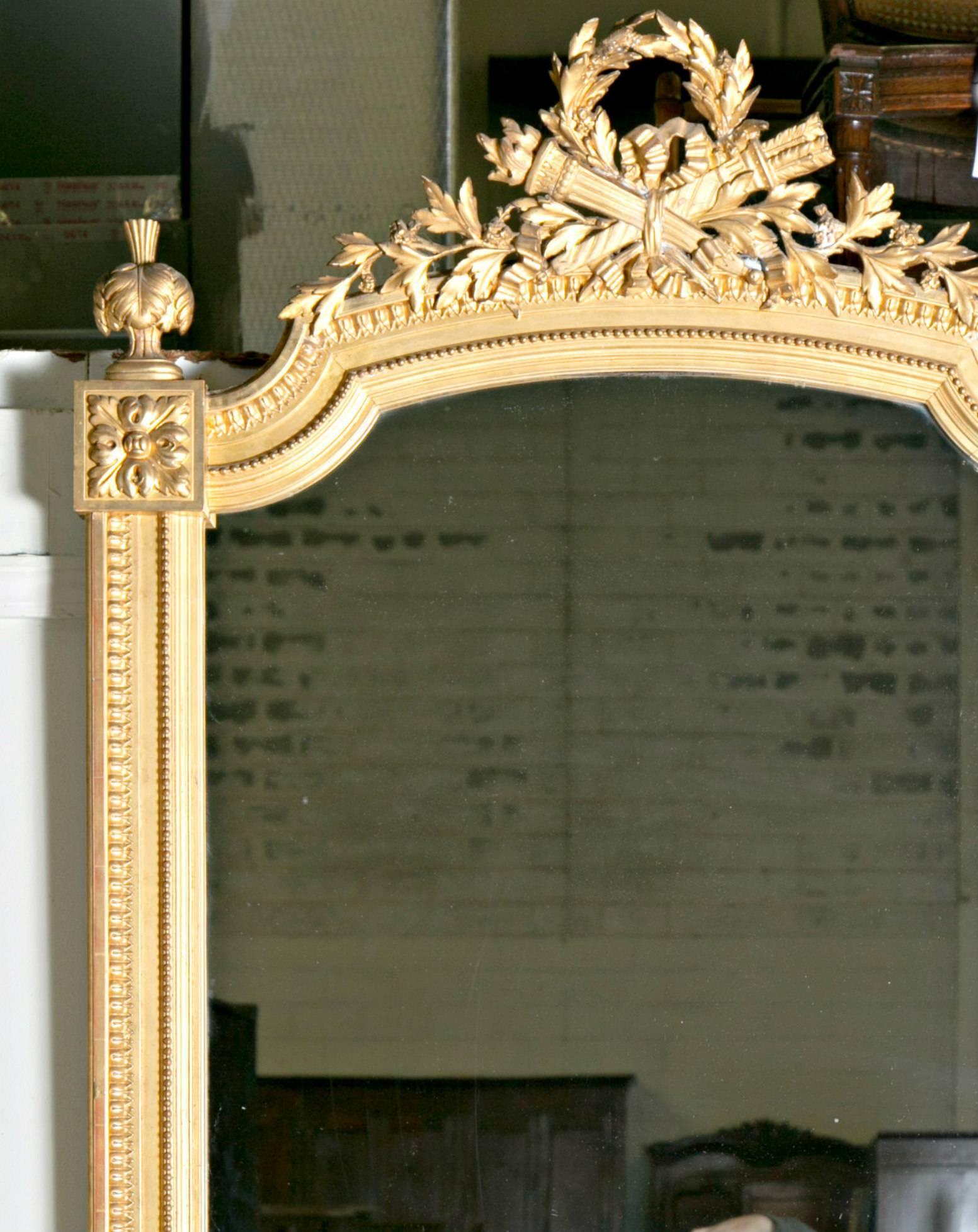 Beautiful French Louis XVI style hand-carved neoclassical giltwood mirror having original glass. The intricately carved crest is formed by the twin symbols of Louis XVI - a quiver of arrows crossed with a flambeau - joined by a laurel wreath and bow
