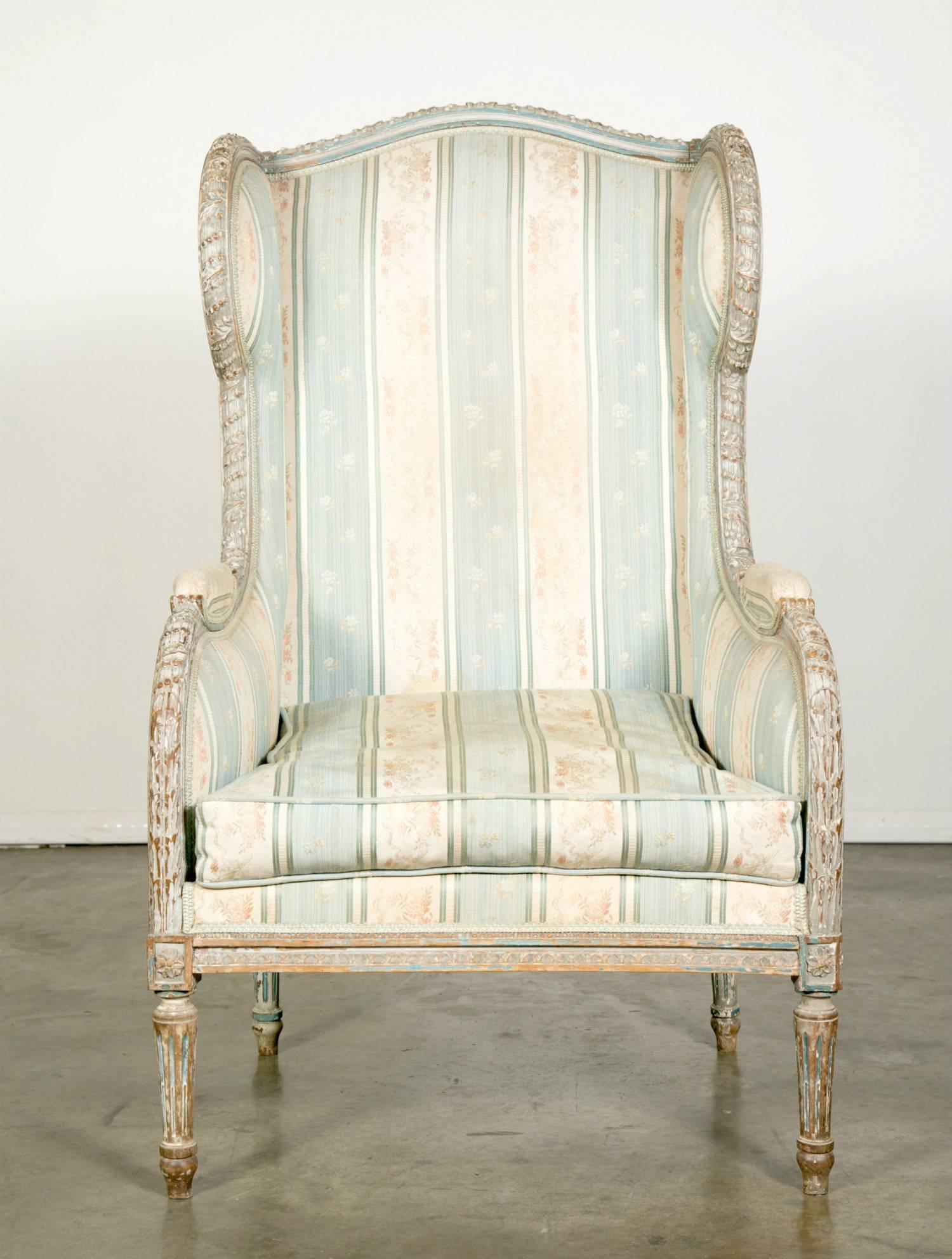 Antique French Louis XVI style Bergère à Oreilles, circa 1880, in original paint featuring wonderful hand-carved neoclassical details carved into the frame with upholstered back, arms, seat, and loose down cushion. Curved wingbacks terminating into