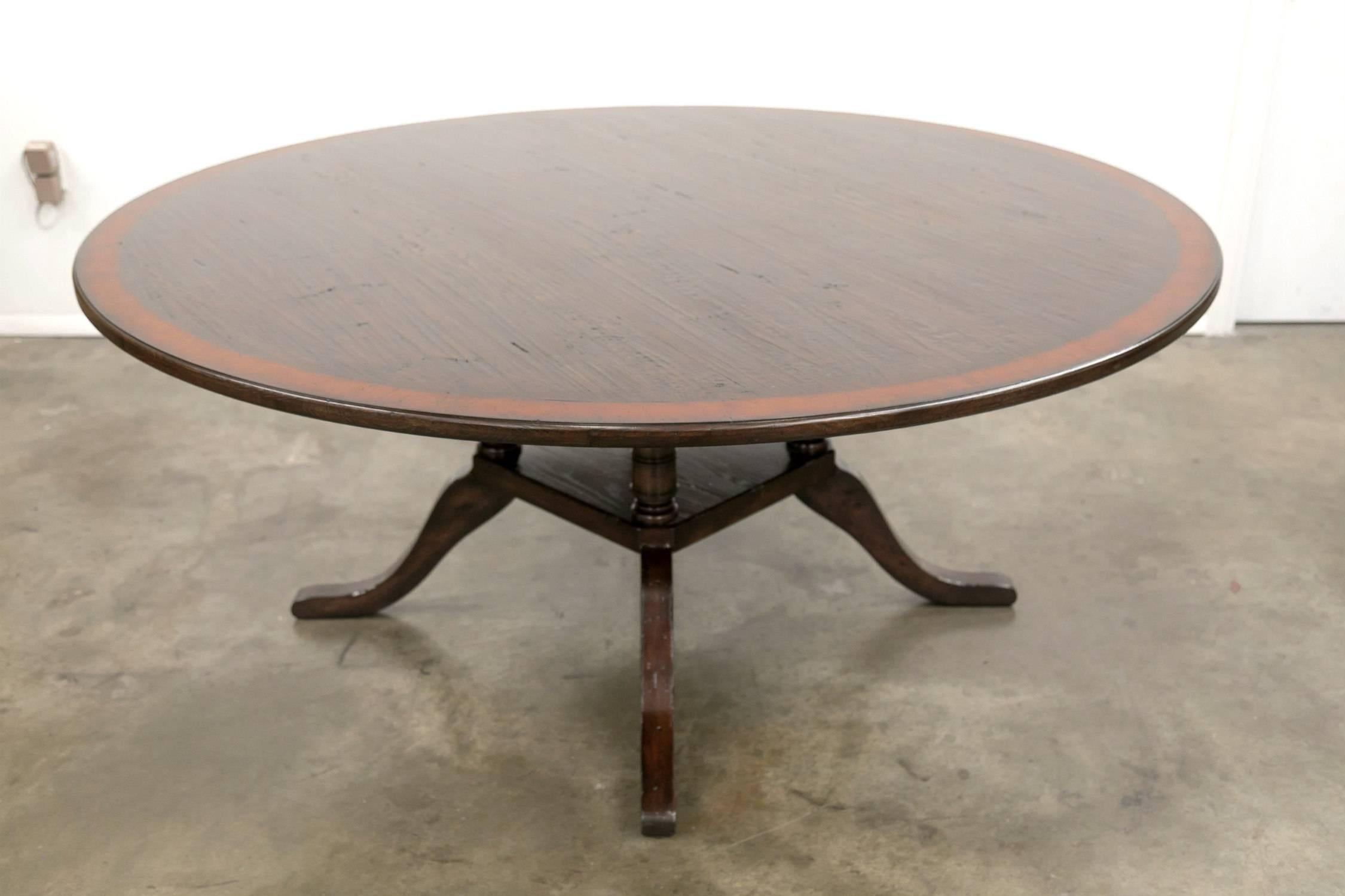 A Classic Georgian style pedestal dining table, handcrafted in England, having a 72-inch diameter, oak top bordered by a rich burled walnut band. Supported by a birdcage pedestal base made of four turned and carved rustic oak columns over a square
