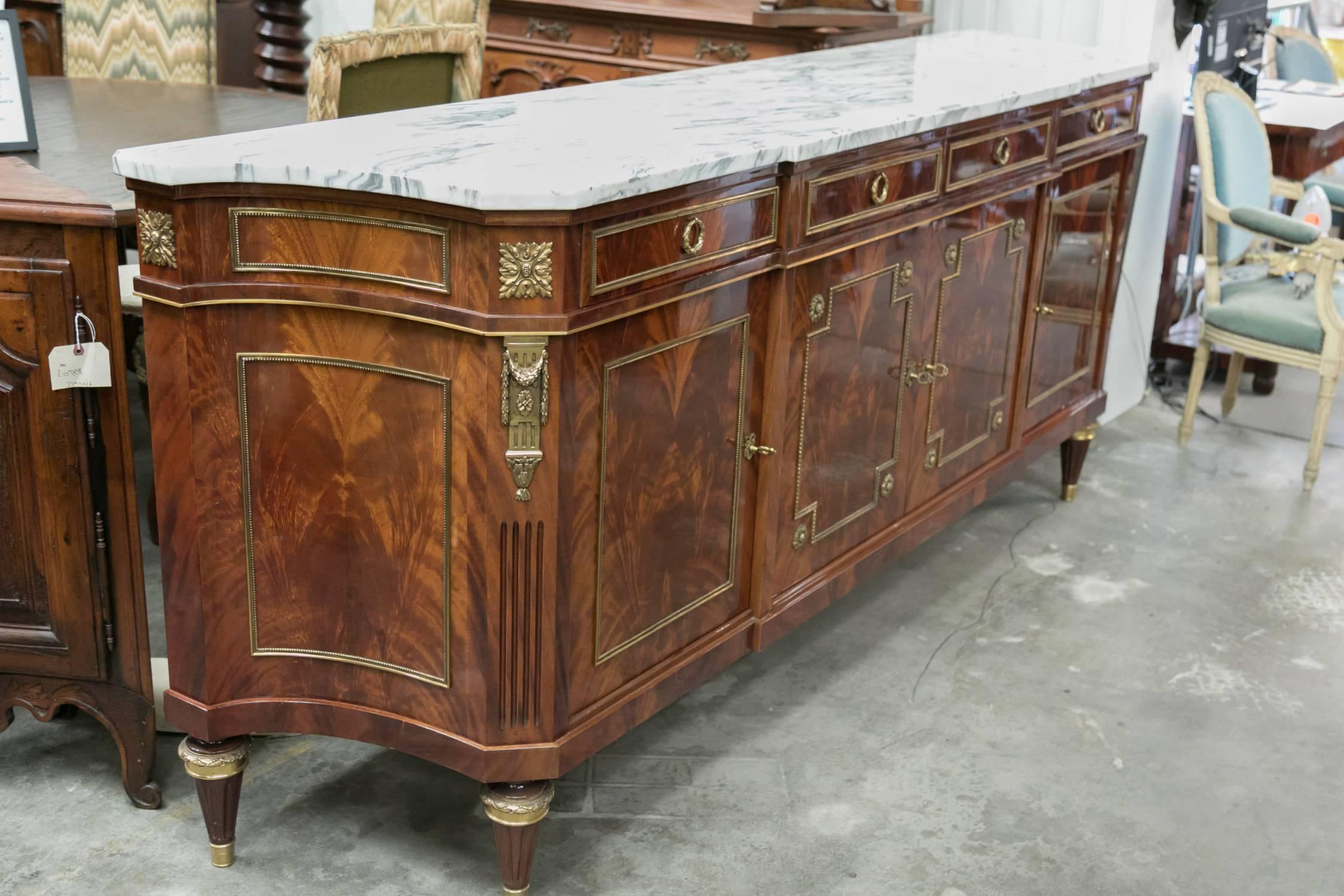 An exceptional and stunning French Louis XVI style enfilade of solid Cuban flamed mahogany with a bookmatched front, having a lustrous French polish, the original thick, moulded Carrara marble top and finely chased bronze ormolu mounts and brass