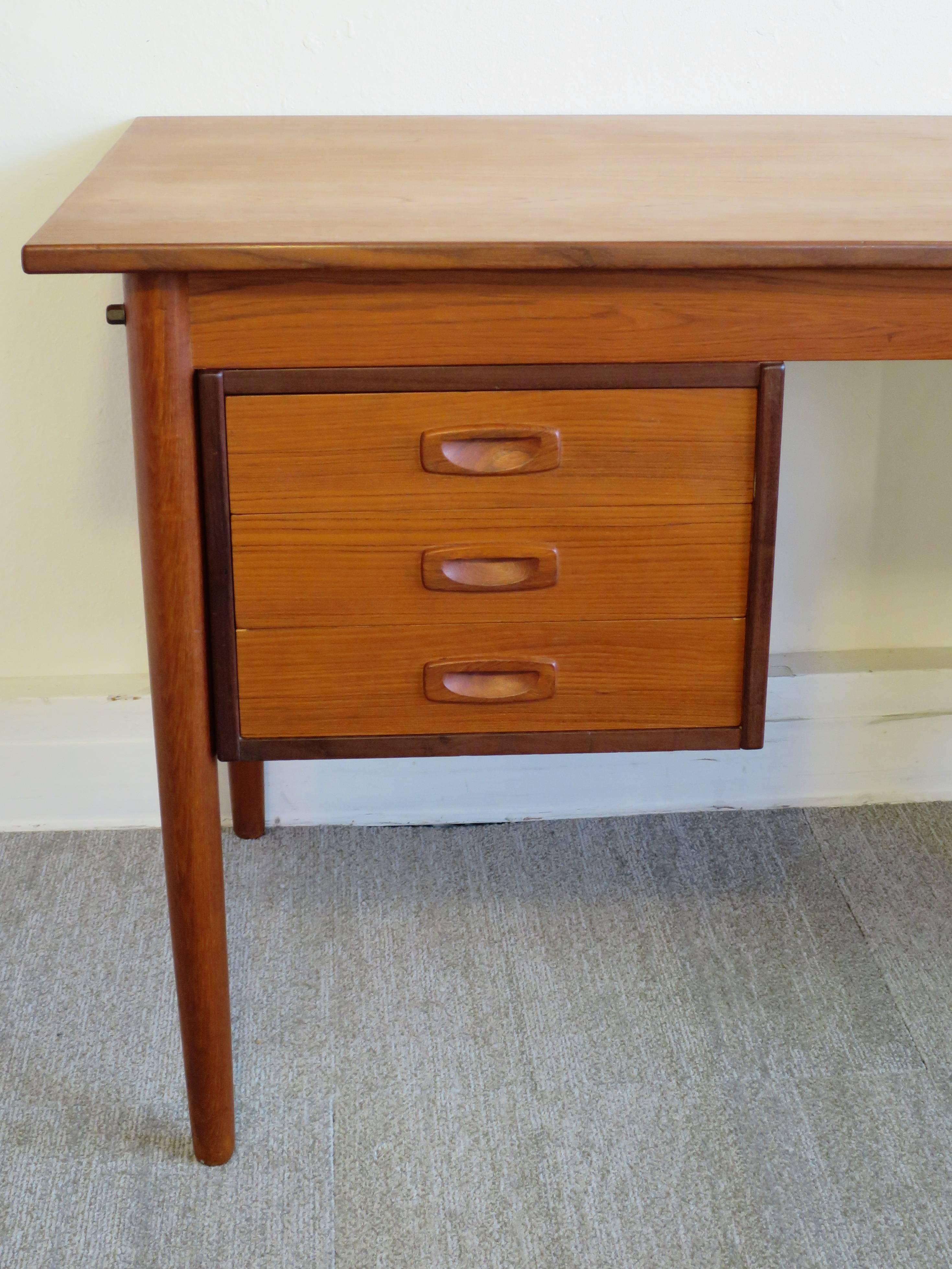 Danish Modern teak desk by Arne Vodder. Has a drop-leaf and finished back with storage. The three drawers can be shifted from left to right. When open the leaf adds 16