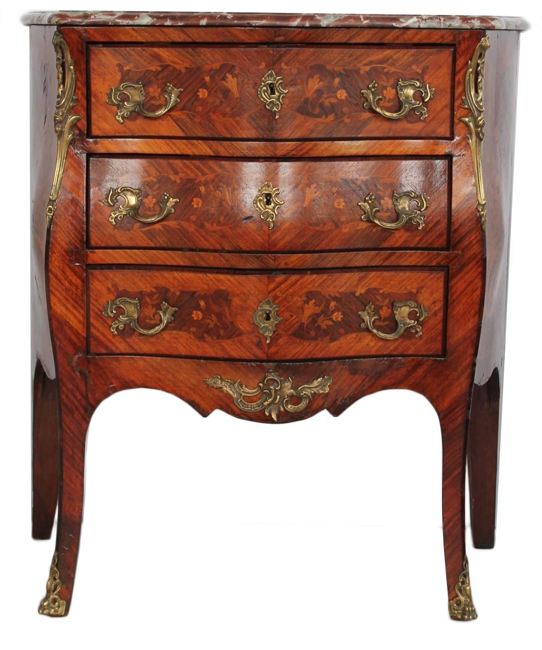 With serpentine rouge marble top over a conforming case, with three floral and foliate inlaid long drawers and shaped frieze, raised on splayed legs ending in bronze sabots.