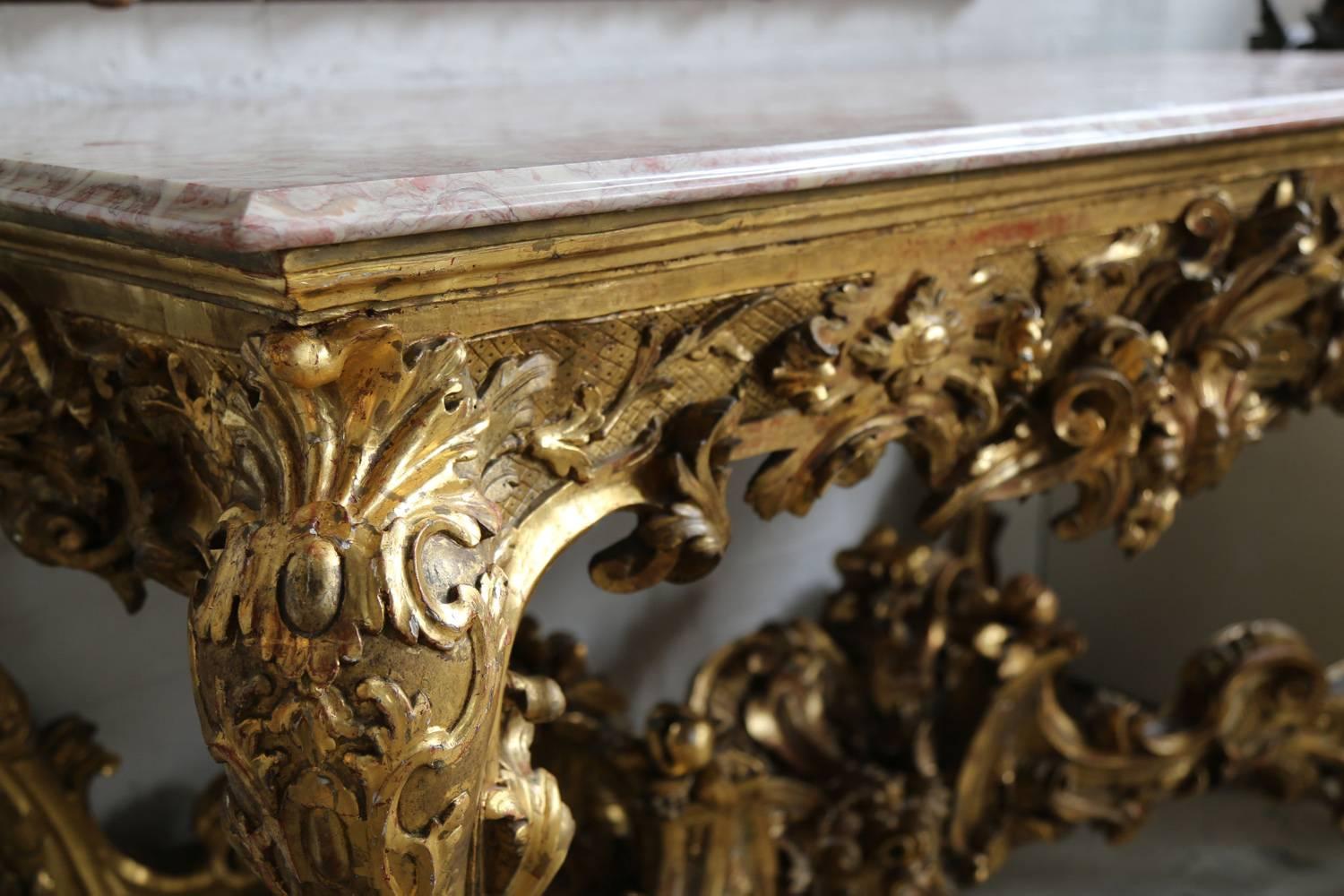 An Italian carved and gilded wood console table, late 18th/early 19th century.
The rectangular pink marble top over an elaborately carved and gilded base, the frieze centered by a foliate form on a lattice and punch work ground, with carved strap