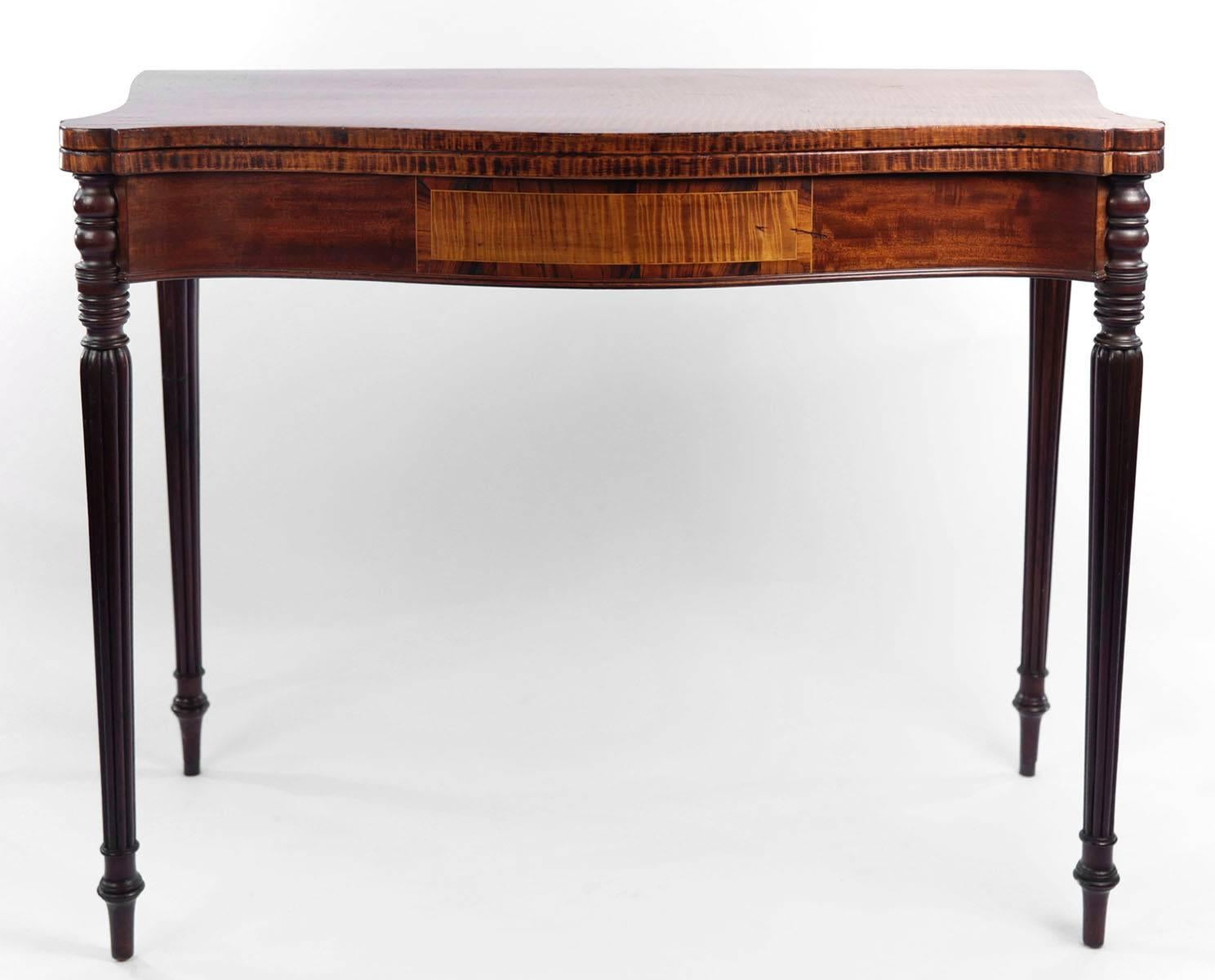 The serpentine shaped top with turret shaped corners, of beautifully figured tiger maple timber, opening to a similarly fine surface, over a conforming frieze with inlaid panel and raised on turned reeded tapering legs.