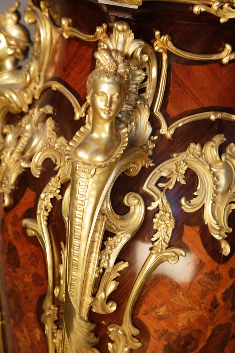 Each with squared fleur de pecher marble top fitted with a gadrooned gilt bronze border centered by floral filled cartouches and scroll forms, the marble tops rotating on a bombe pedestal base, the case fitted with gilt bronze cabriole mounts with