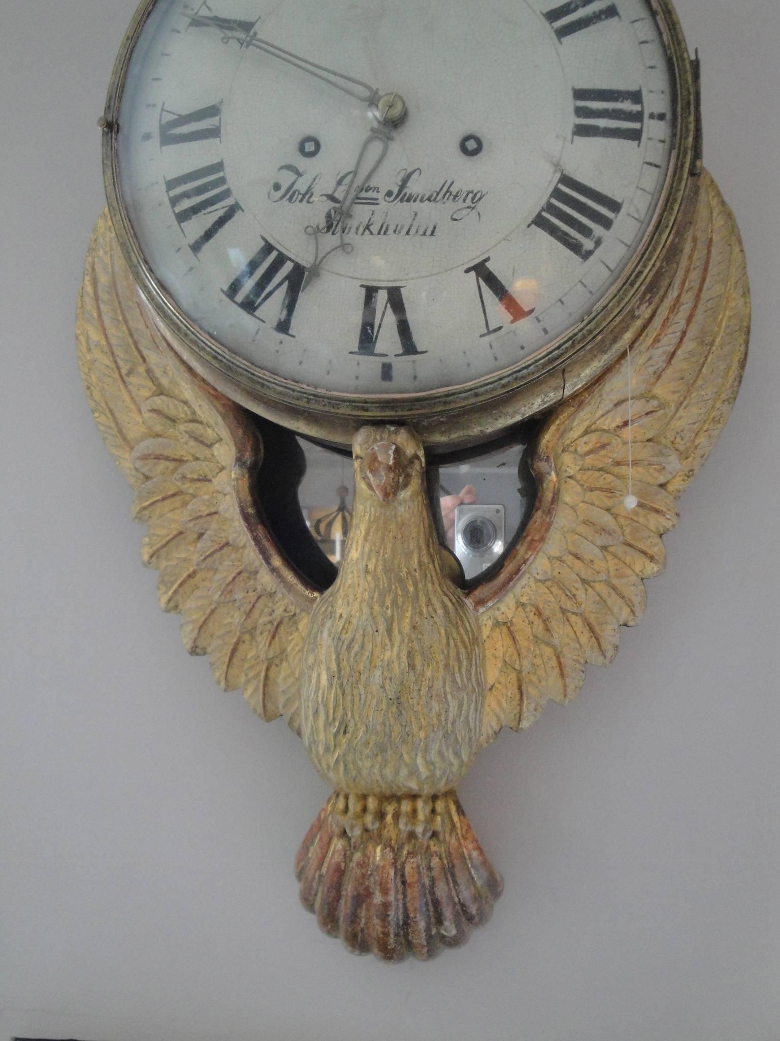 18th century Gustavian wall clock atop a carved and gilded eagle with porcelain clock face. Signed 