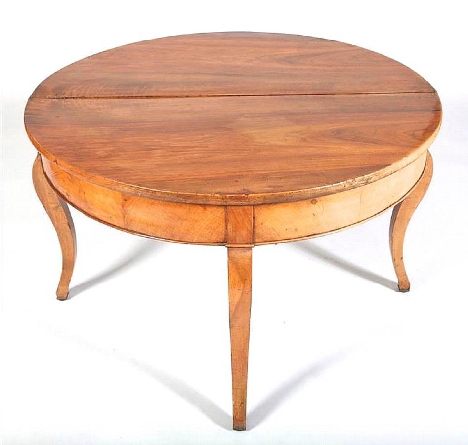 A honey colored walnut demilune table resting on boldly formed squared and tapered cabriole legs which terminate in brass feet. The fourth leg pulls out revealing a drawer and serves as the support for the top when opened to form a round center or