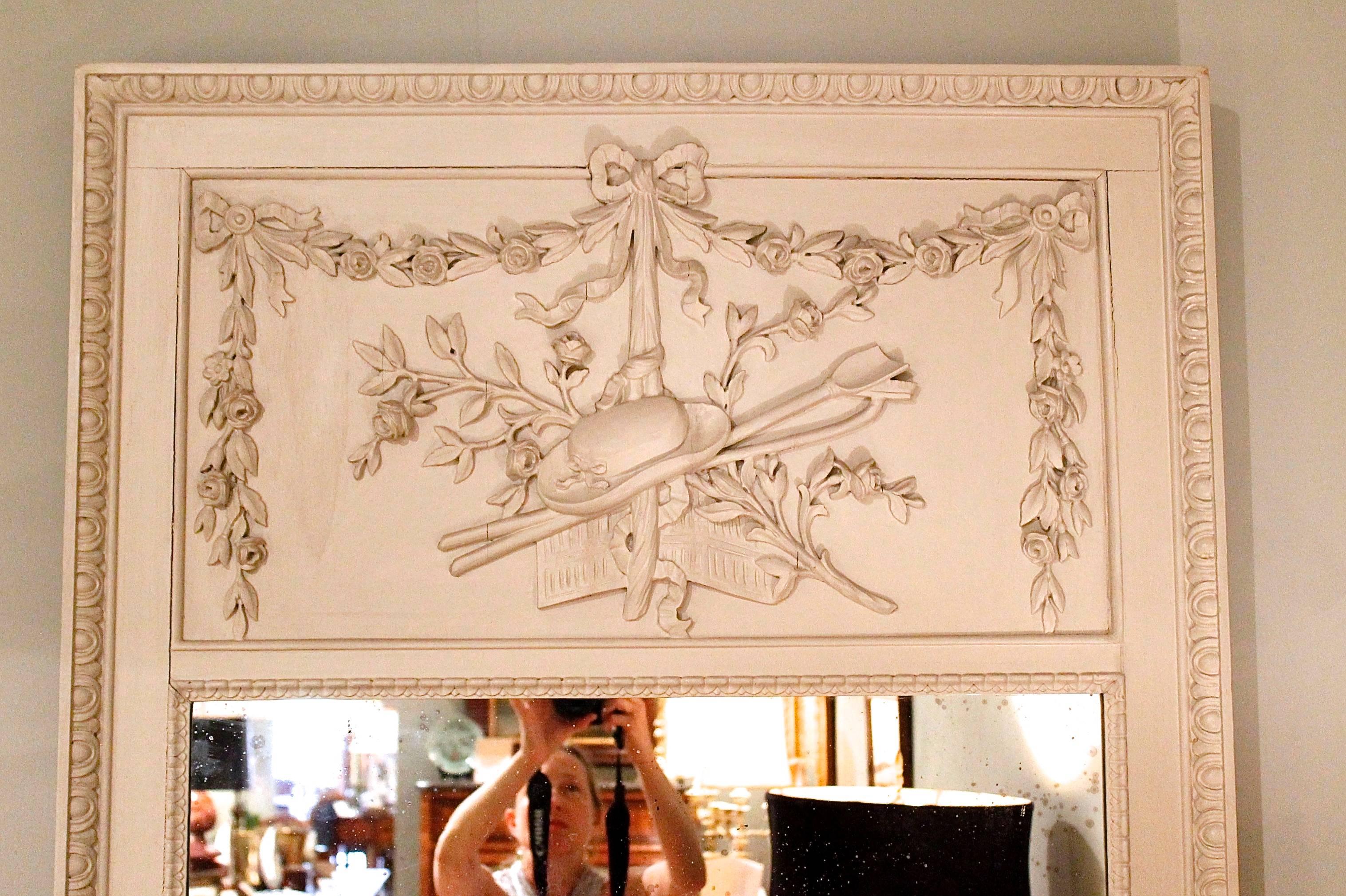 A lovely French trumeau mirror ornamented with applied carving depicting rose garlands, garden tools and a hat, the whole bounded by egg and dart moulding and with low relief waterleaf carving around the mirror.