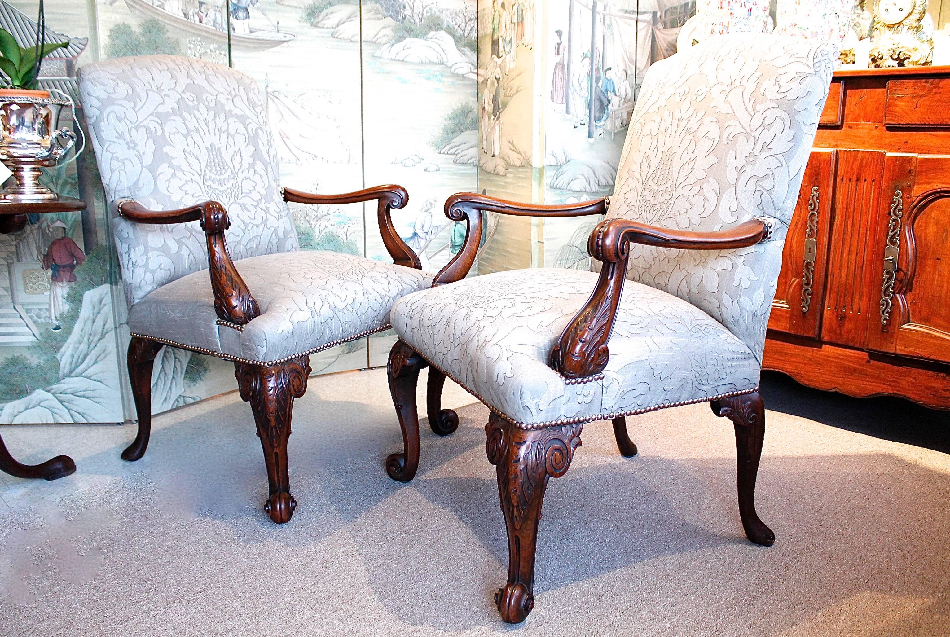 A fine pair of mahogany library chairs in the George III manner, of ample proportions with particularly well carved cabriole legs in front, terminating in scroll feet, and with backswept legs in the rear. The arms are likewise nicely carved with