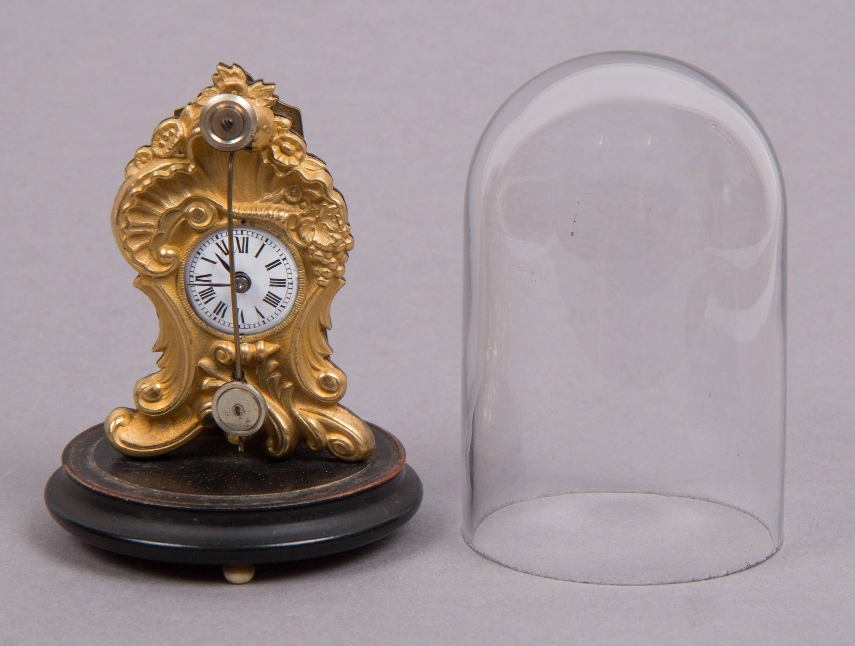 Height: 9.7 cm (with bell jar), diameter base: 6.5 cm.
Fire gilt brass case, bell jar, enbonised wooden base, enamel dial, hook escapement.