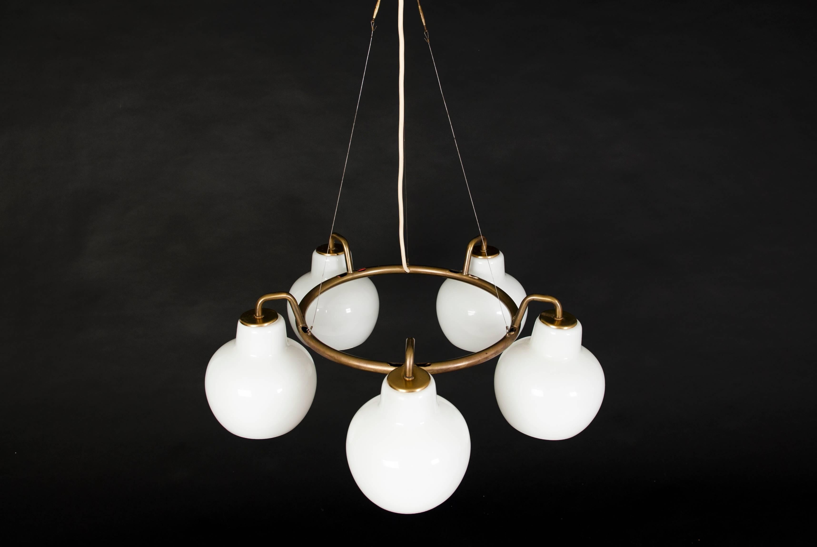 Vilhelm Lauritzen.

Christiansborg chandelier. Brass ring, five branches with shades of multi-layer opal glass. 

Manufactured by Louis Poulsen.
 