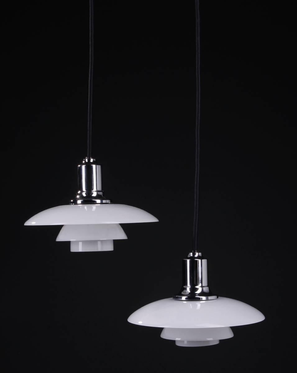 Poul Henningsen PH 2/1 pendants. 
Fitted with one E27 socket, white opal glass shades, black fabric cords. 
Produced by Louis Poulsen. Ø 20 cm. Minimal wear.