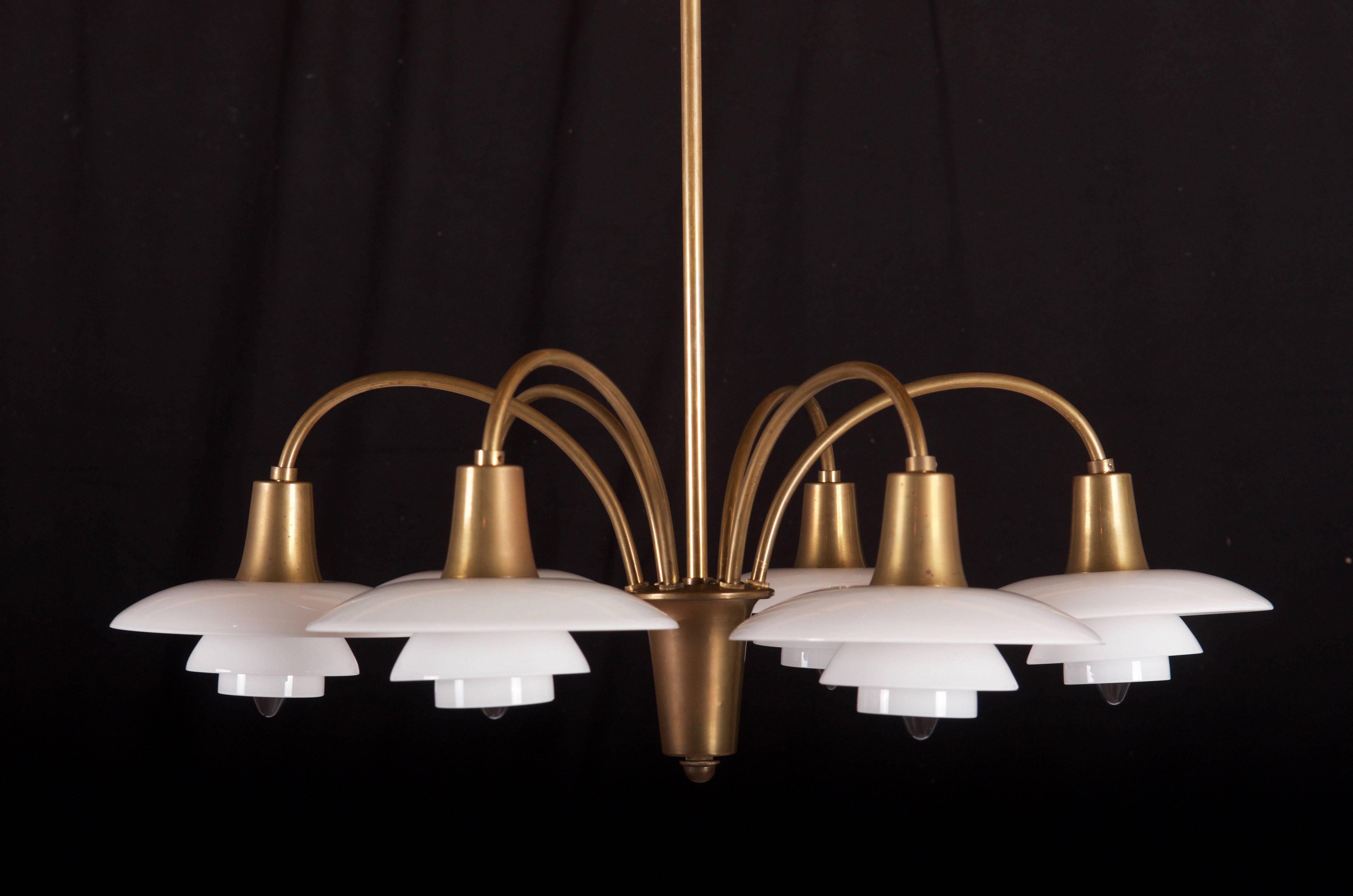 Originally designed by Poul Henningsen for Louis Poulsen in the 1930s. An exceptional example of the design. Bombardment chandelier with six branches, brass frame, conical socket covers, wire shade holders with 2/1 opal glass shade sets. This
